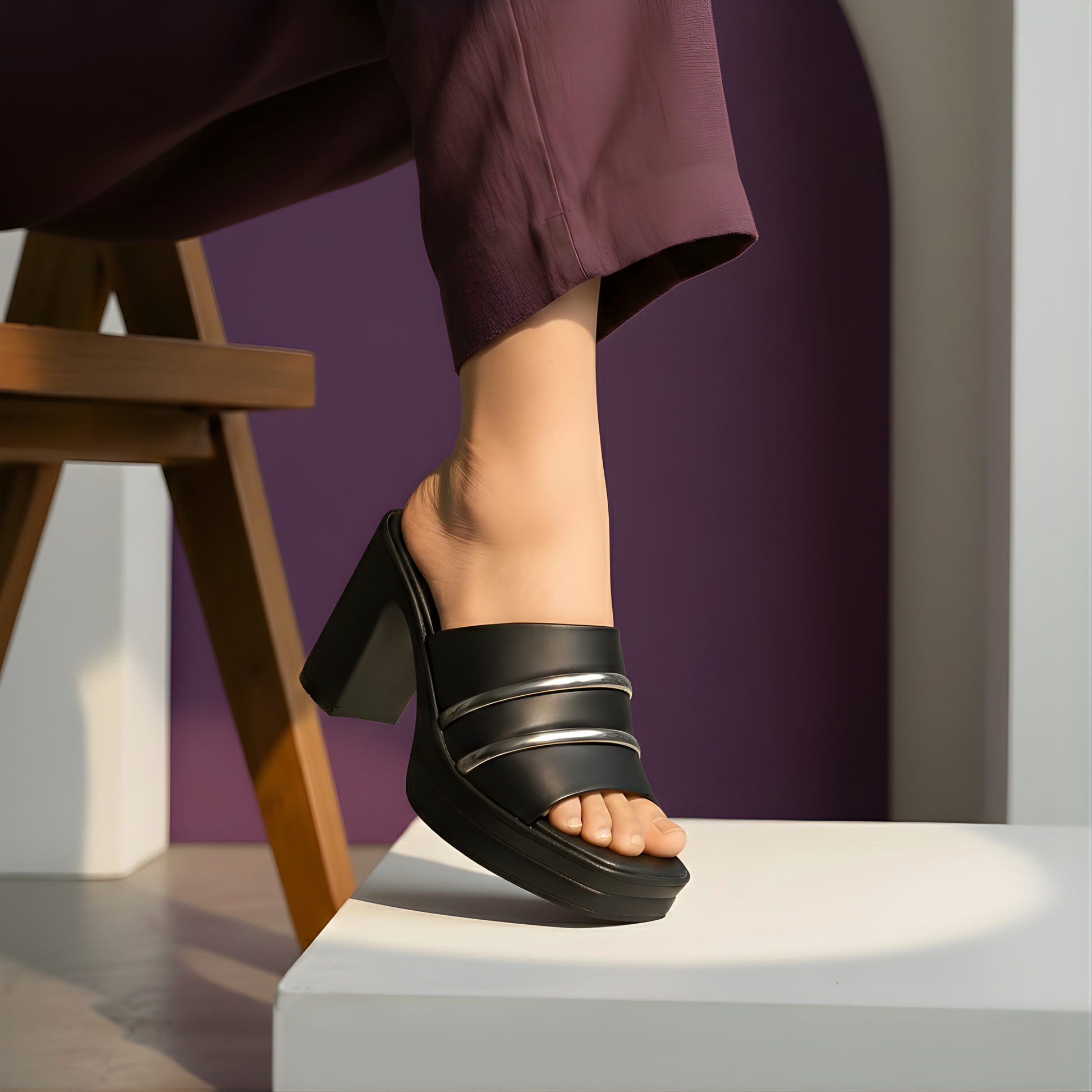 Side view of a person wearing black chunky platform mules with silver strap details, styled with purple trousers and a minimalist background
