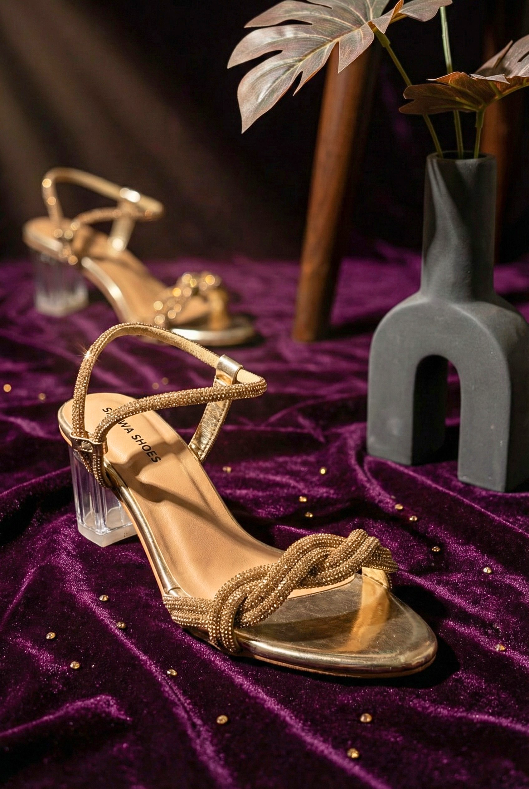 Gold braided rhinestone heels with clear glass block heel on purple velvet background.