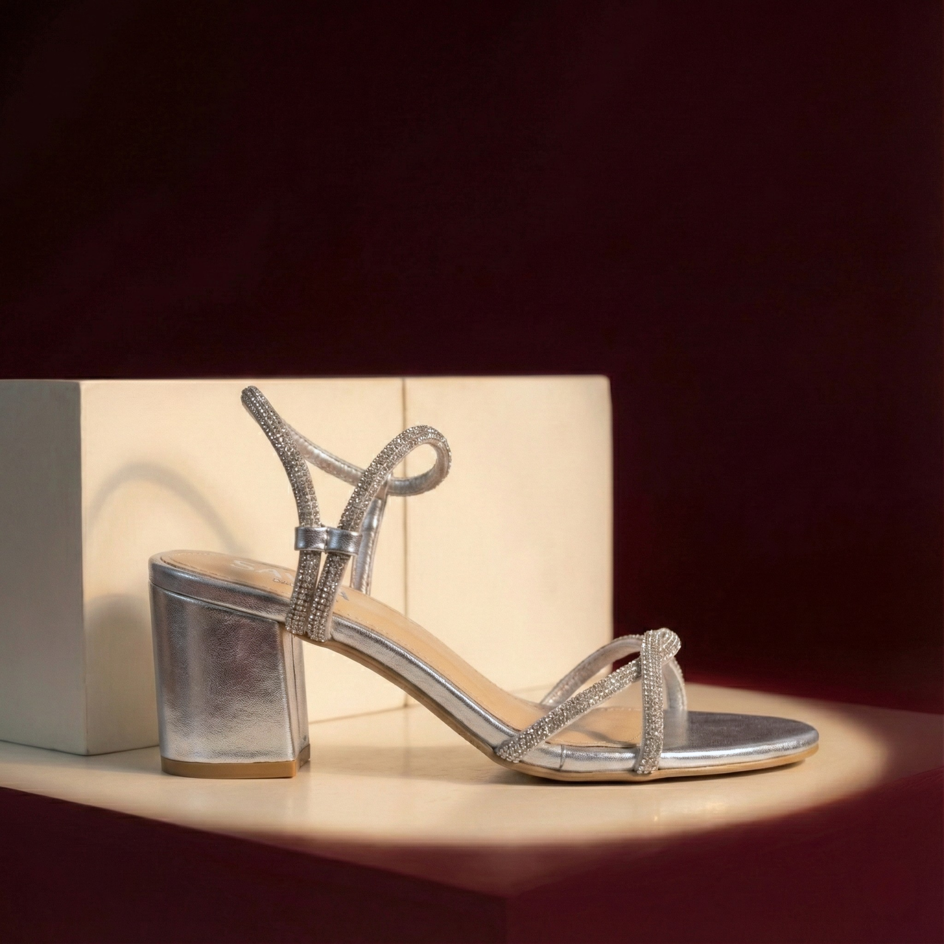 Silver high-heeled sandal on a reflective surface with a dark background