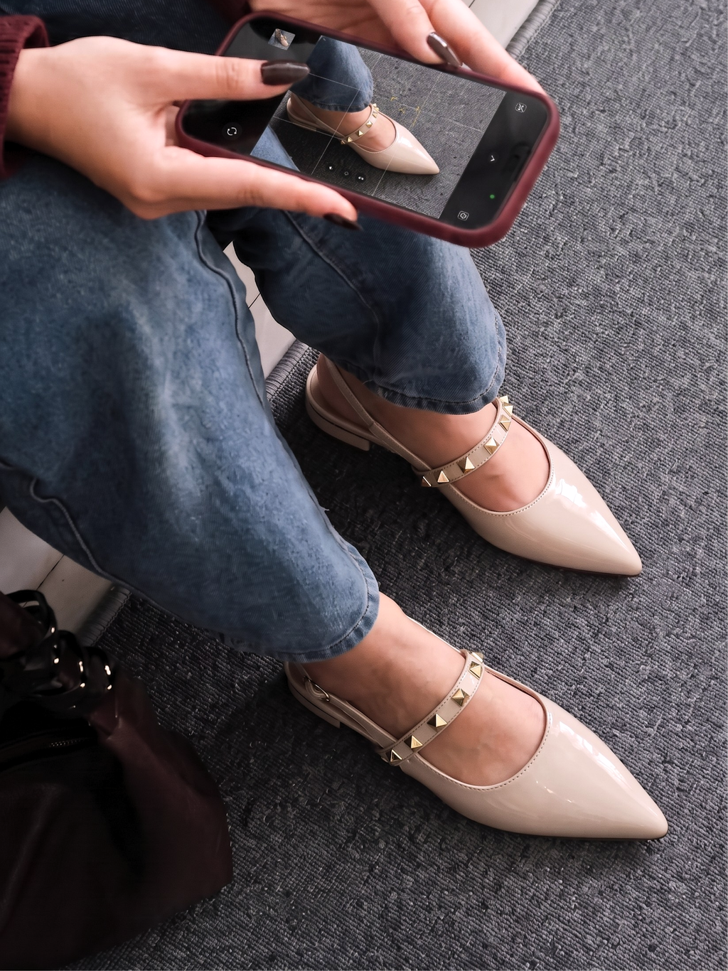 Pair of beige patent pointed-toe slingback pumps with gold pyramid stud details displayed on a grey textured rug