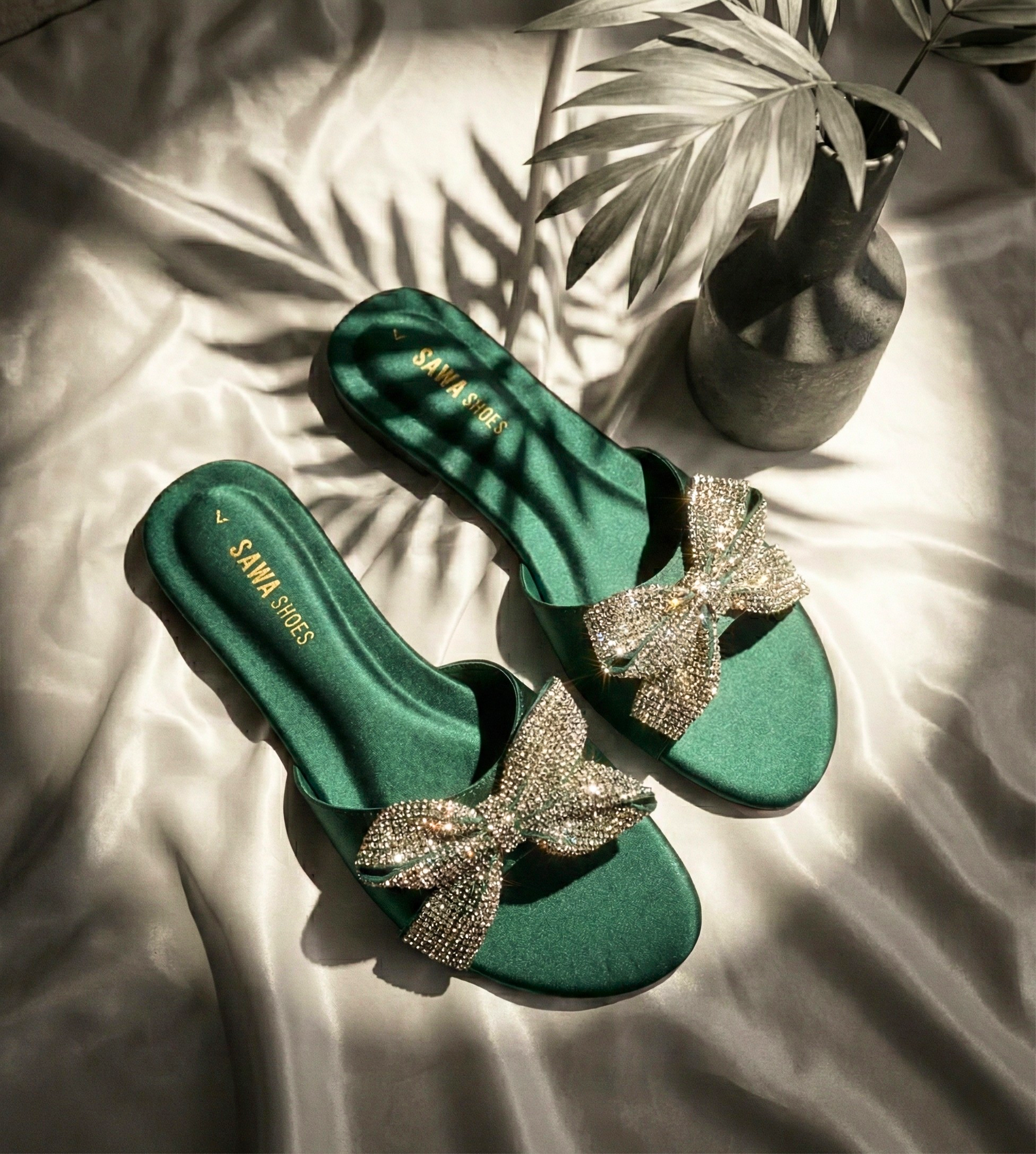 Pair of Sawa Shoes emerald green satin flats with shimmering crystal bows and gold branding.