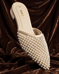 Side view of woman wearing cream pearl-embellished low block heel mules paired with maroon trousers.