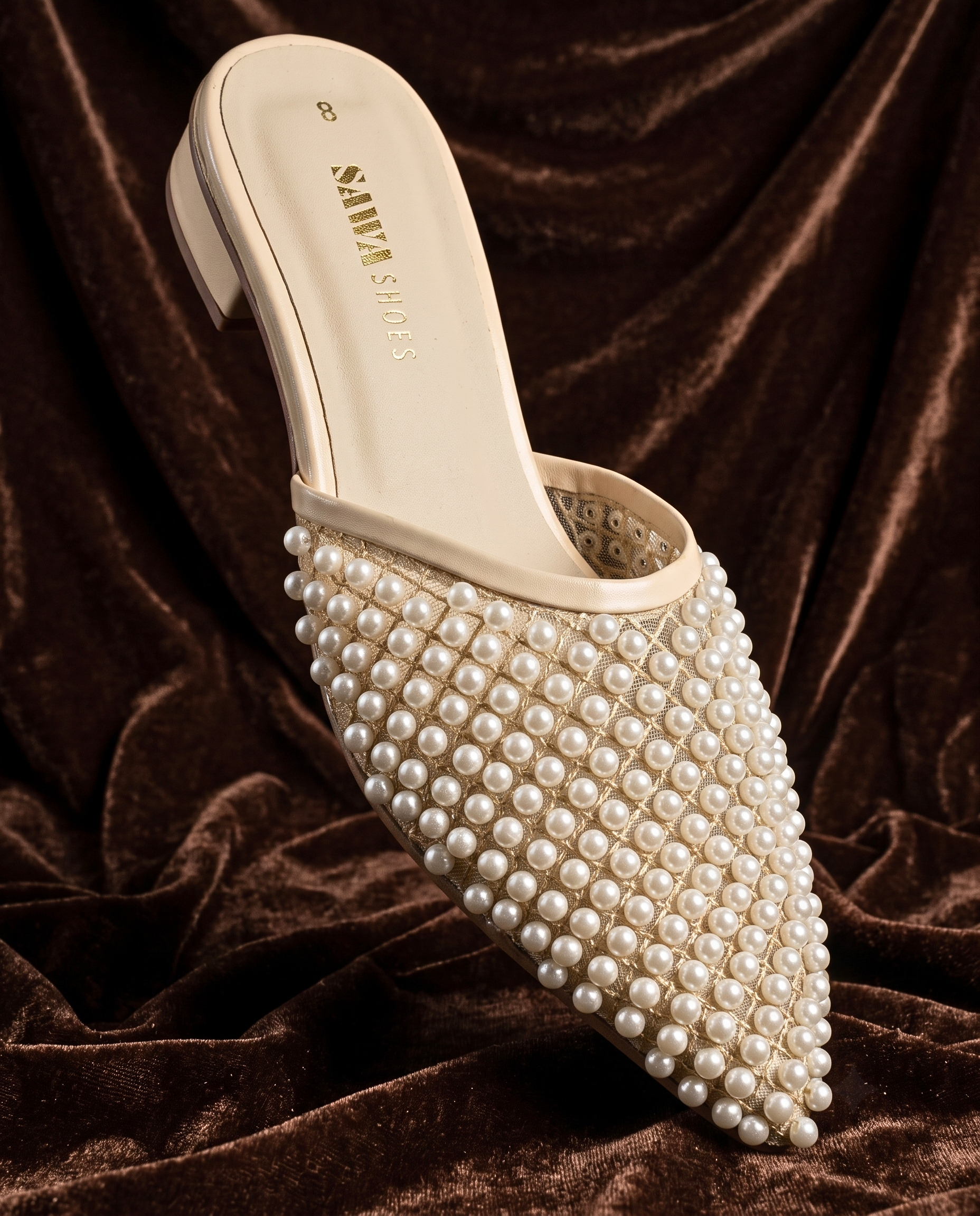 Side view of woman wearing cream pearl-embellished low block heel mules paired with maroon trousers.