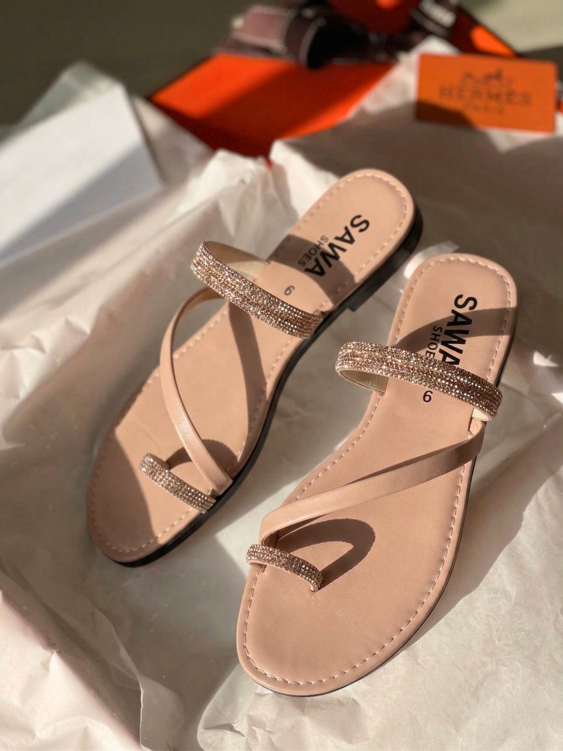 Nude flat sandals with rhinestone embellished straps and toe-ring design on white tissue paper background.