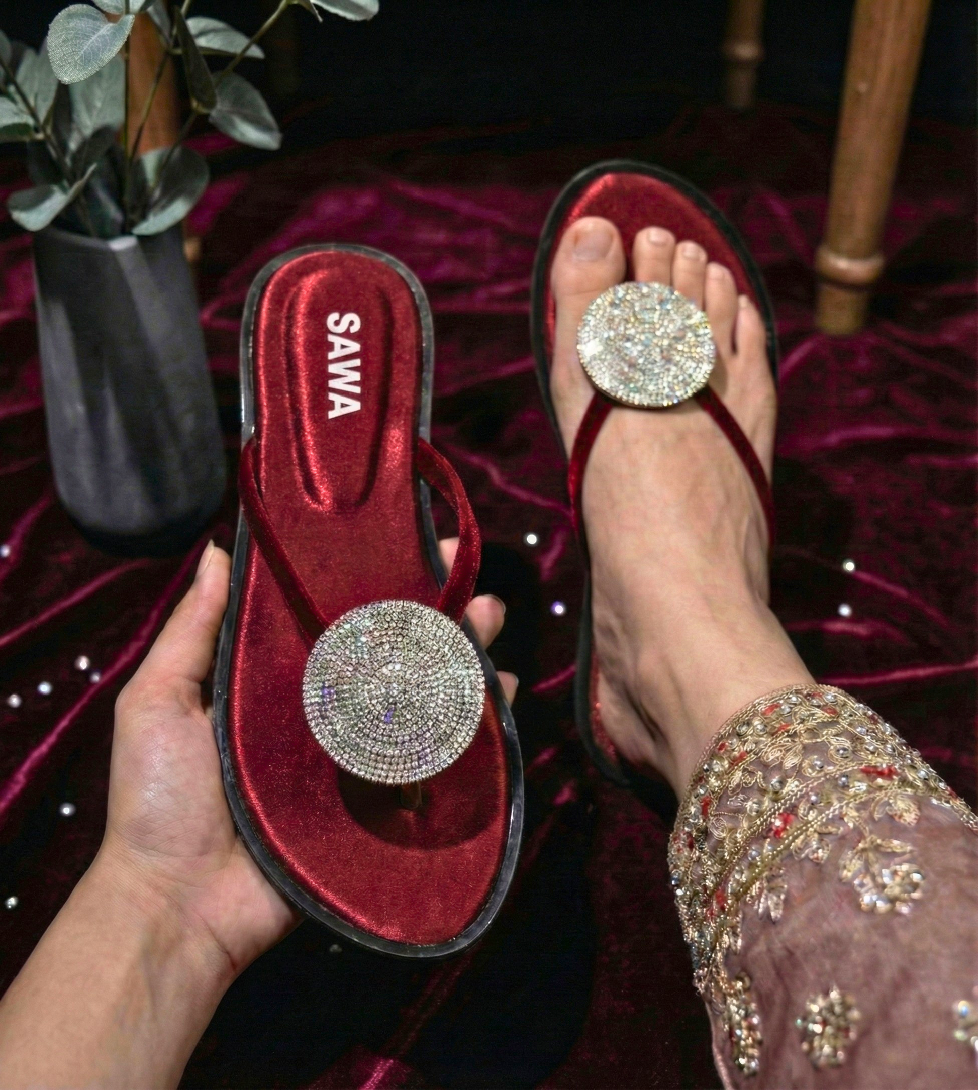 SAWA festive flat sandals in burgundy velvet featuring a large circular crystal-encrusted medallion on the thong strap, styled with embroidered ethnic wear.