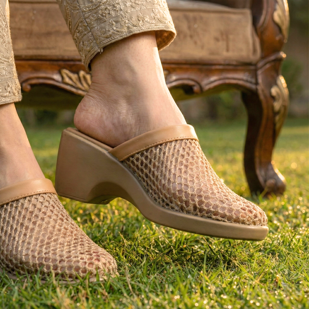 Person wearing beige mesh shoes on grass with a wooden chair in the background