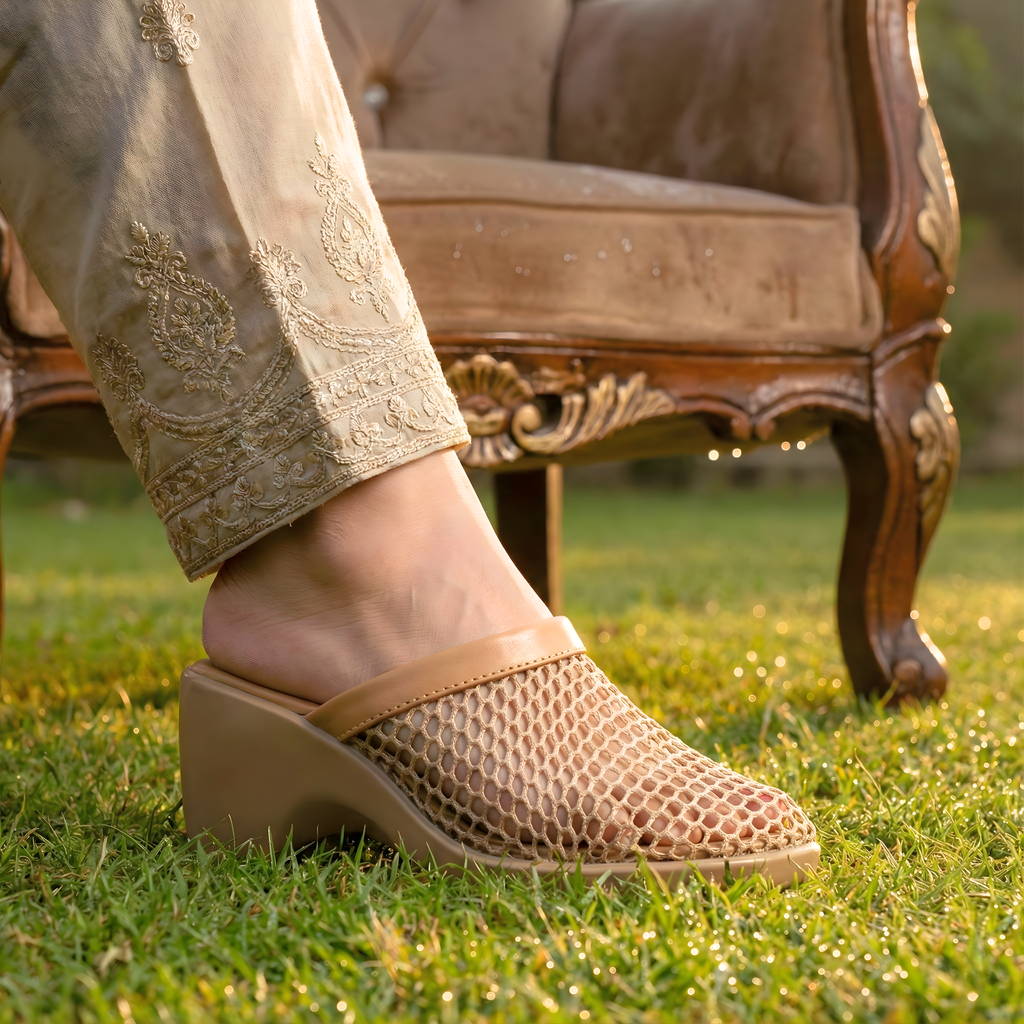 Foot wearing a sandal on grass with an ornate chair in the background