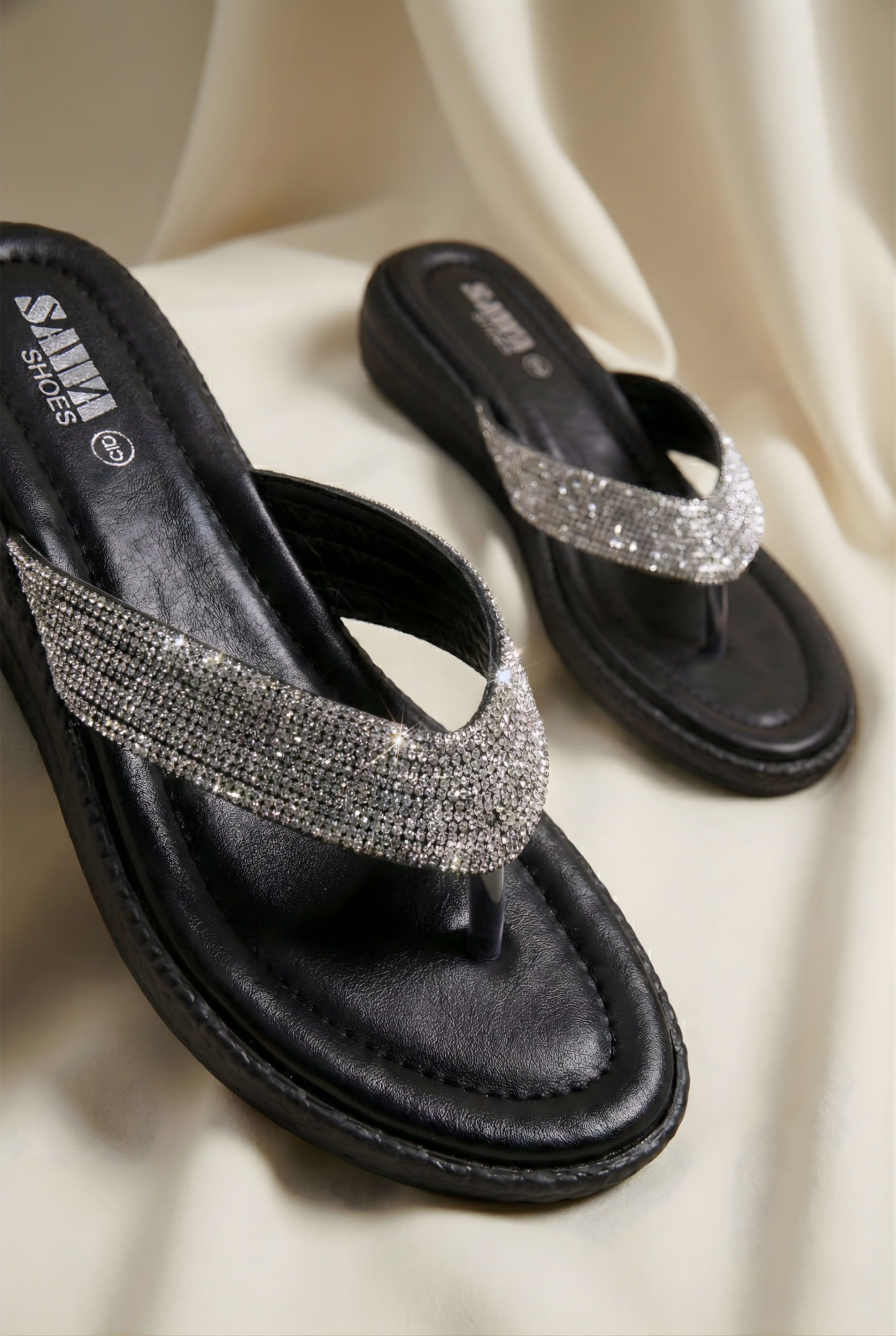 Black sandals with silver embellishments on a beige fabric background