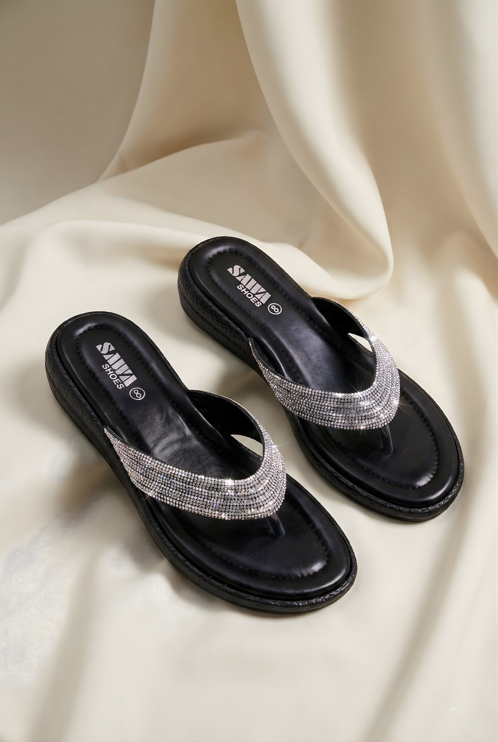 Black sandals with crystal embellishments on a beige fabric background