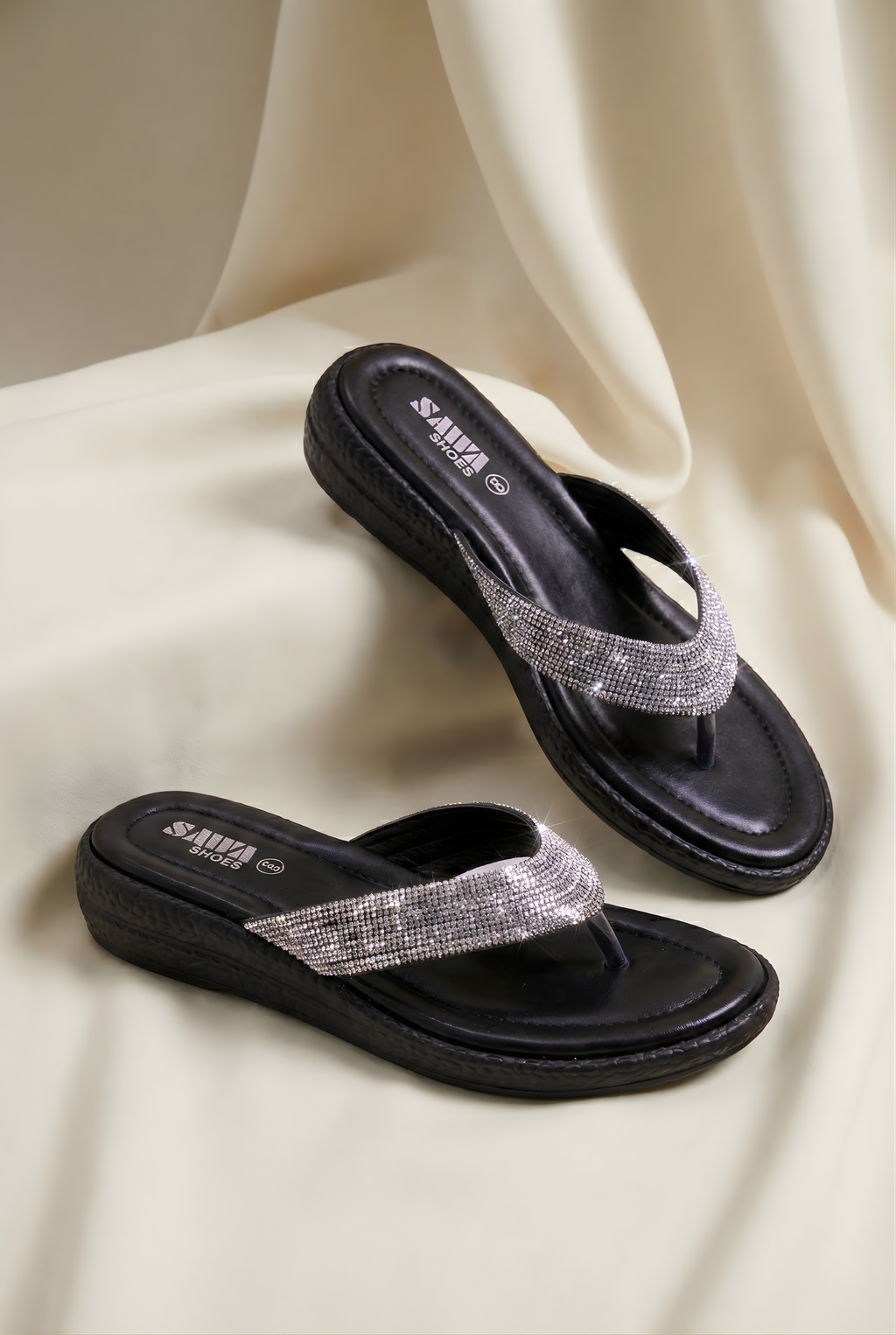 Black sandals with silver straps on a beige fabric background