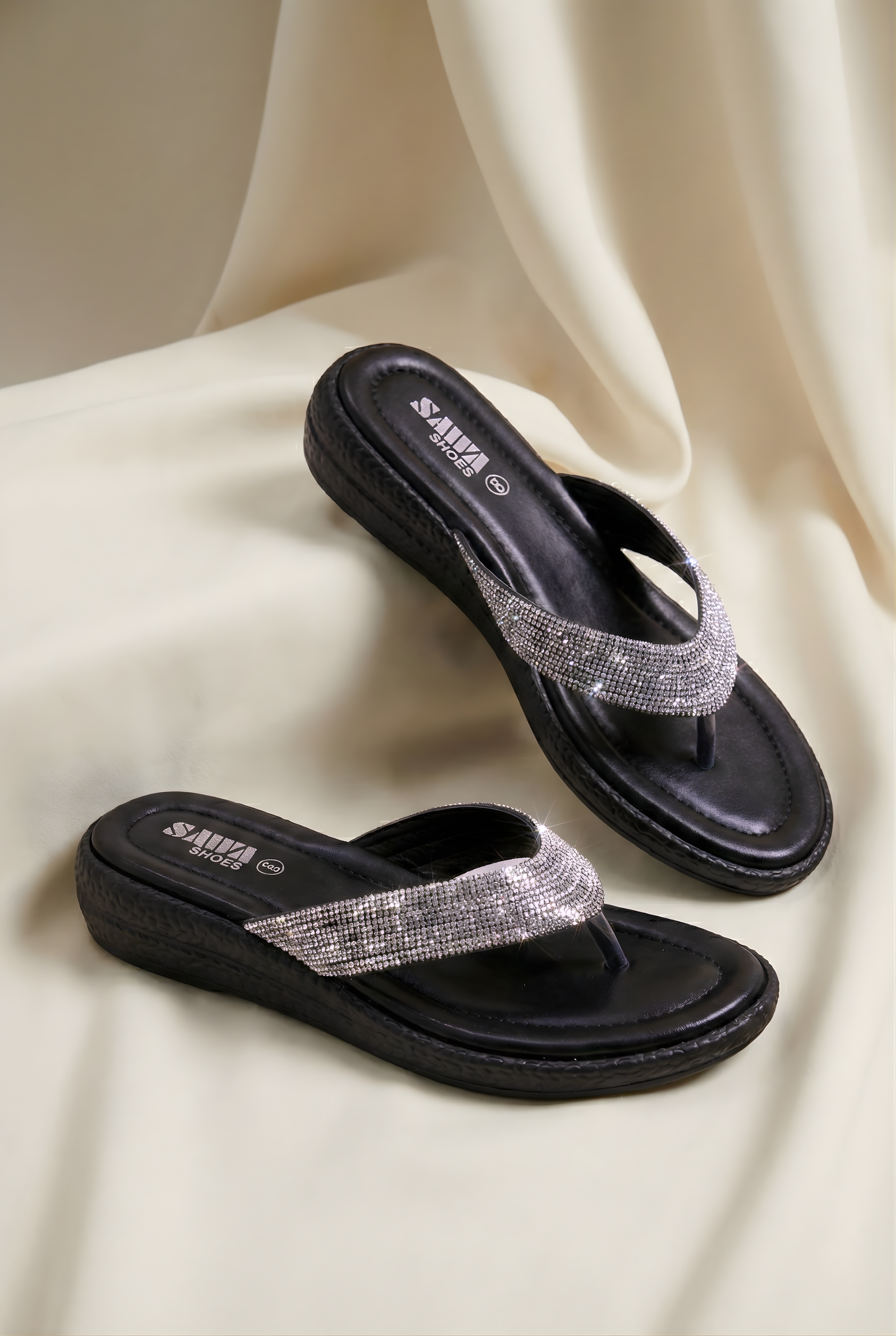 Black sandals with silver straps on a beige fabric background