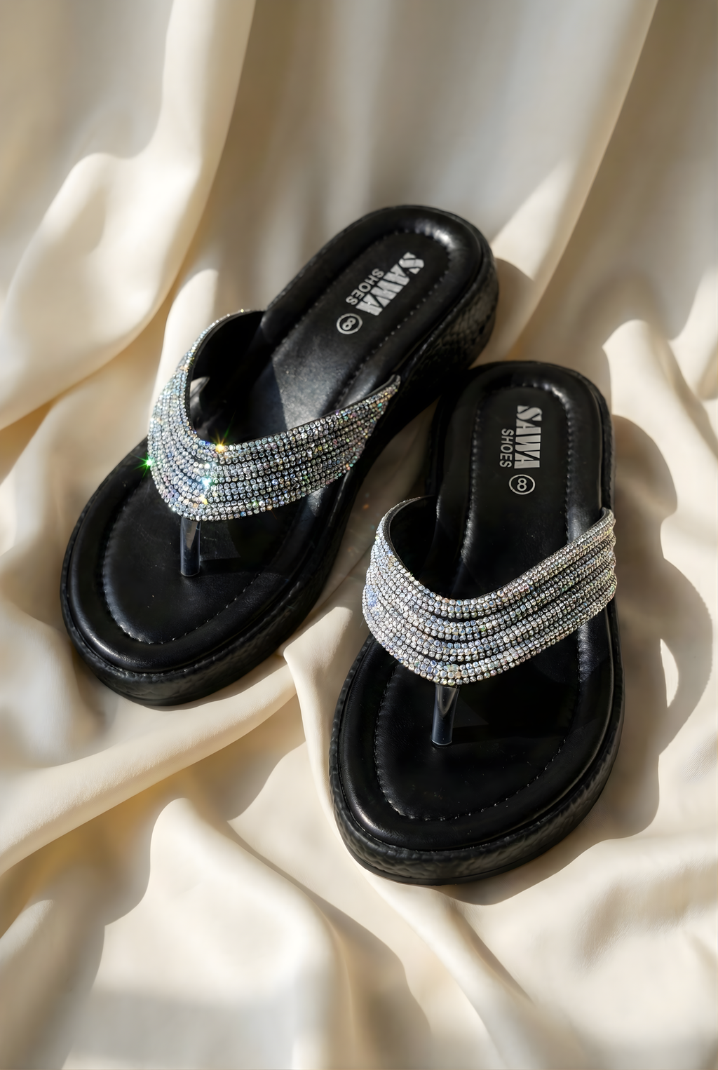 Black sandals with rhinestone straps on a beige fabric background