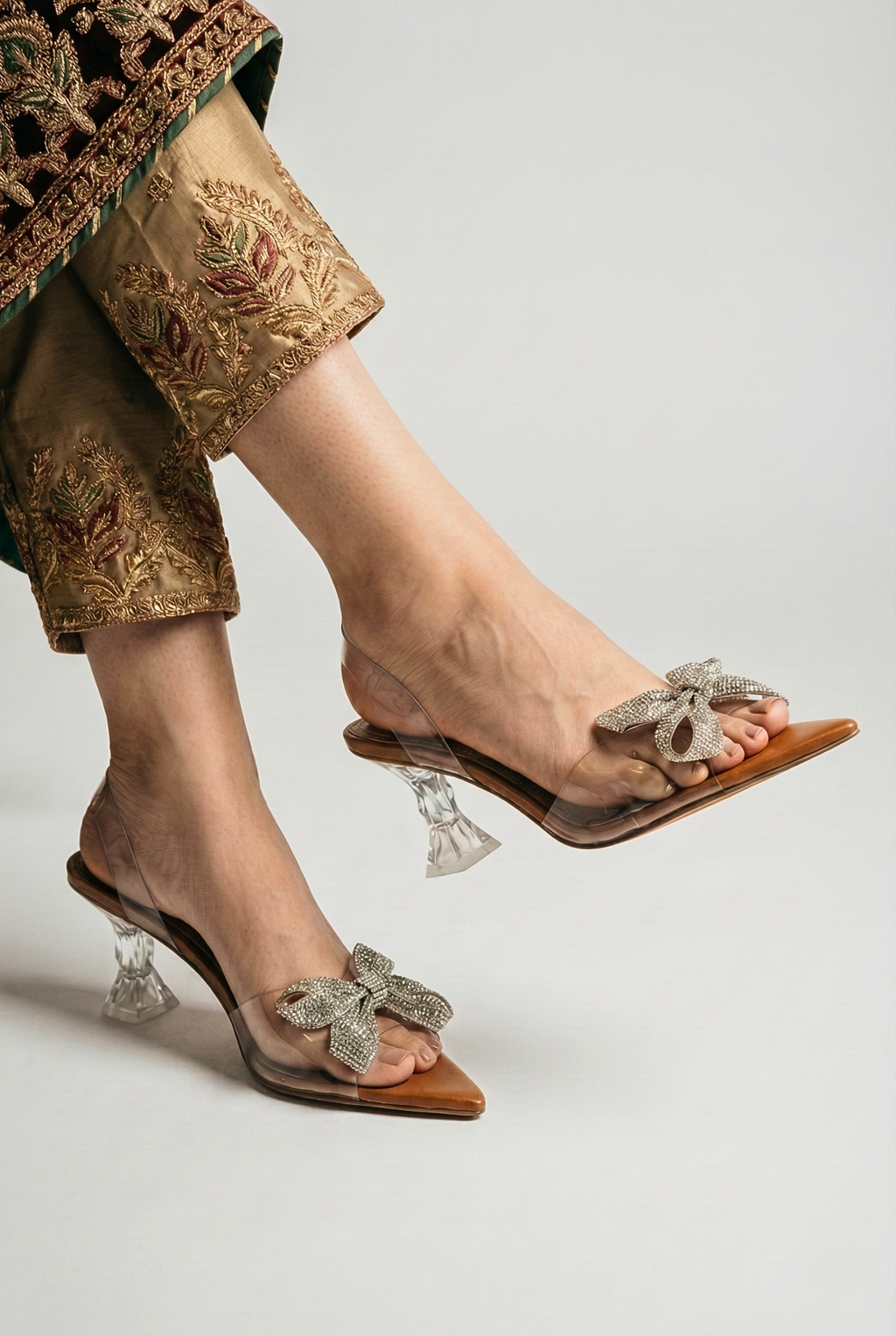 Woman wearing transparent crystal bow heels paired with embroidered Pakistani raw silk trousers for wedding party
