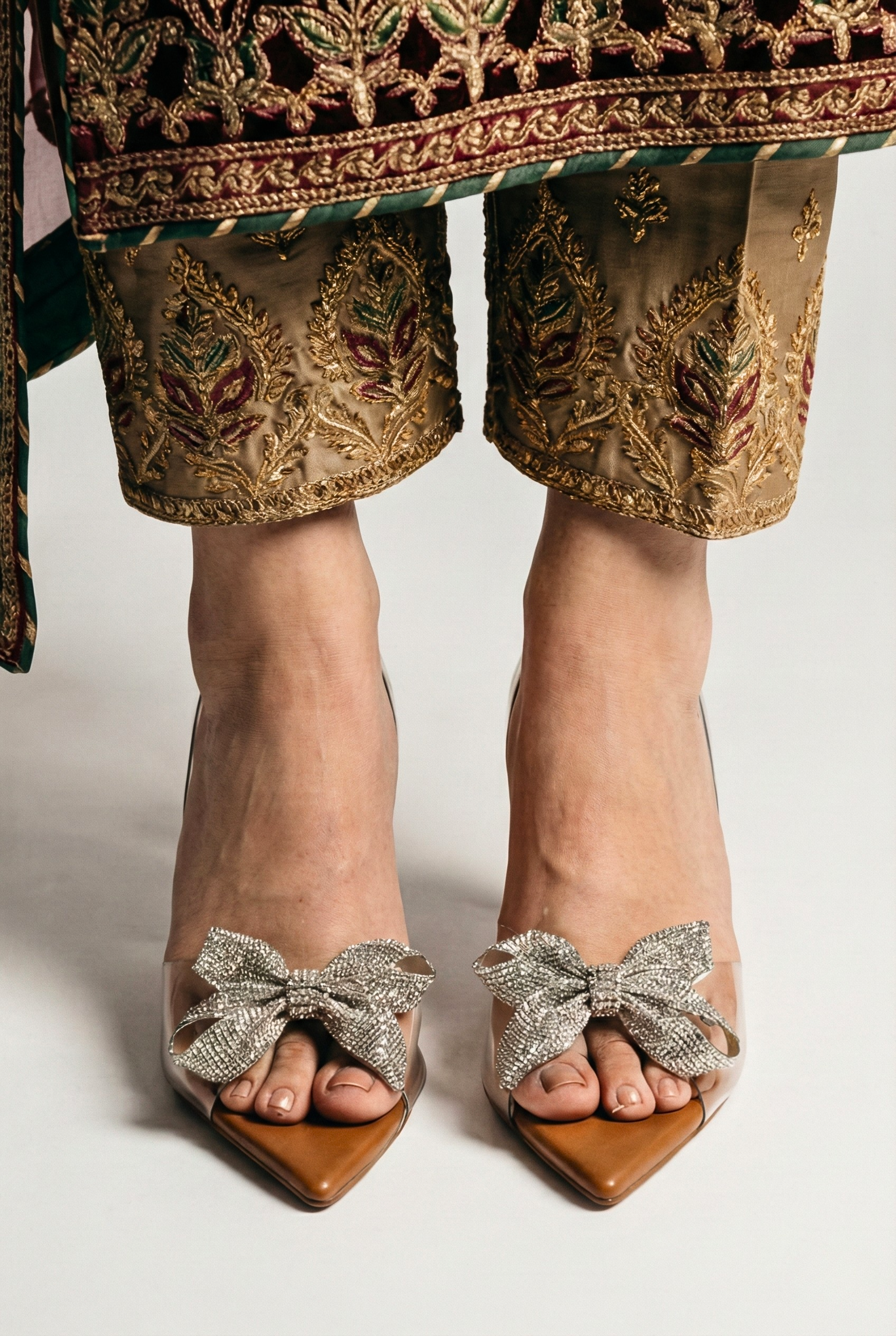 Woman wearing transparent crystal bow heels paired with embroidered Pakistani raw silk trousers for wedding party