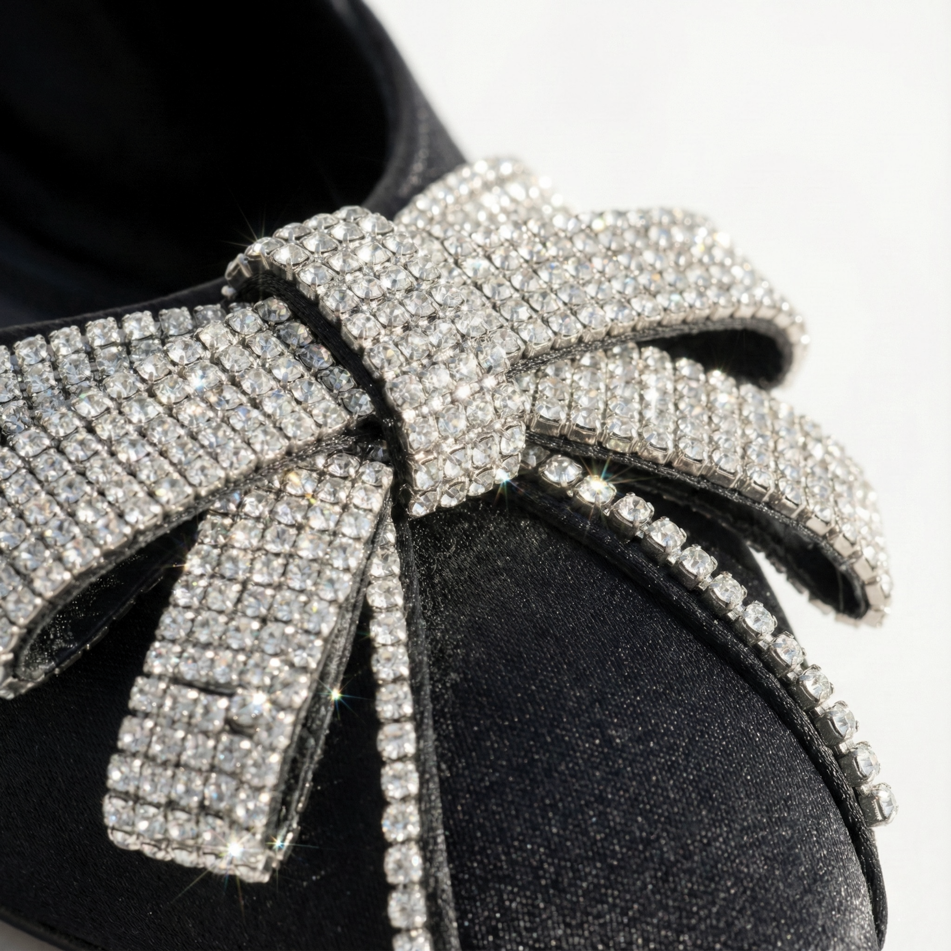 Close-up detail of silver rhinestone-encrusted bow on black fancy party wear shoes.