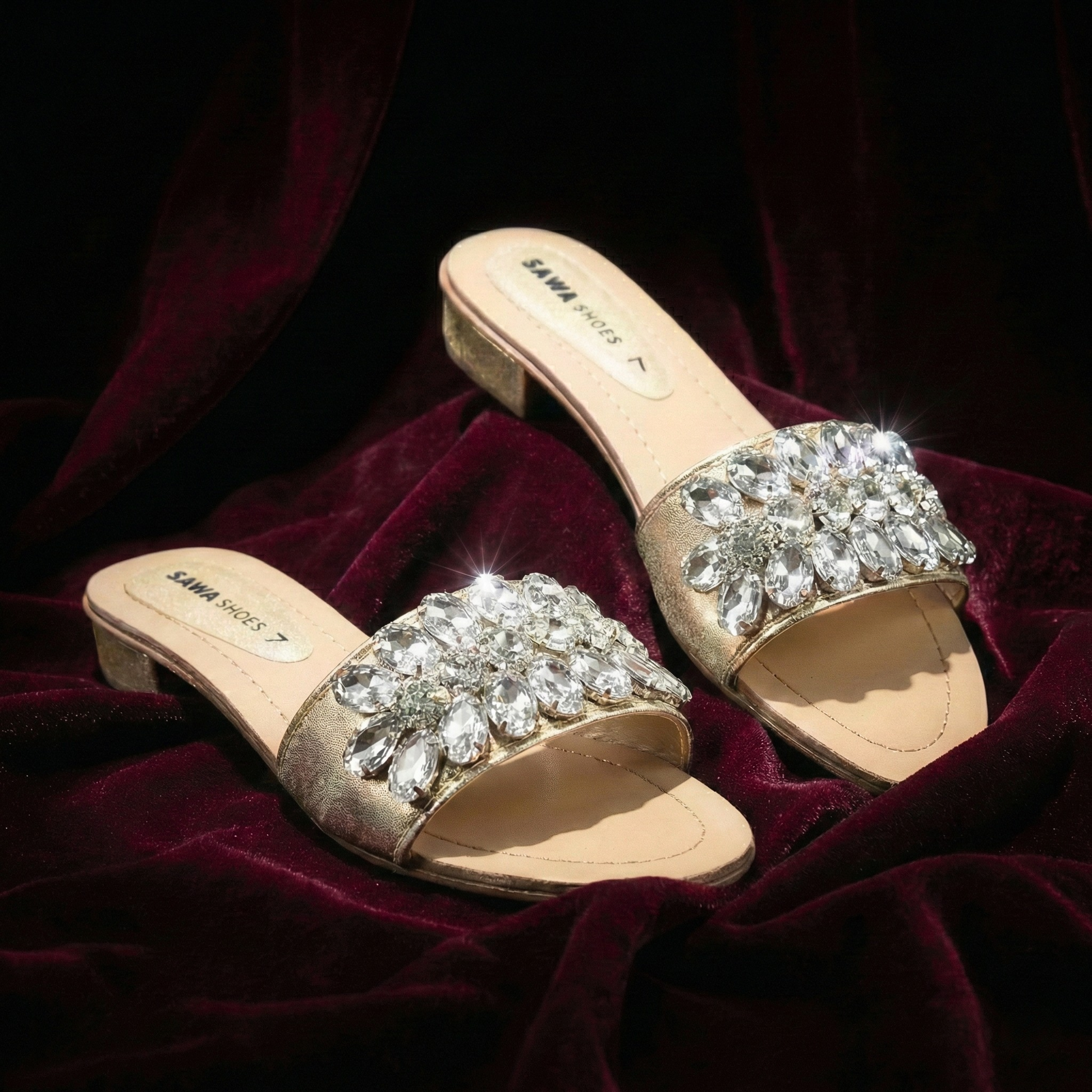 Gold block sandals with crystal embellishments on a dark red fabric background