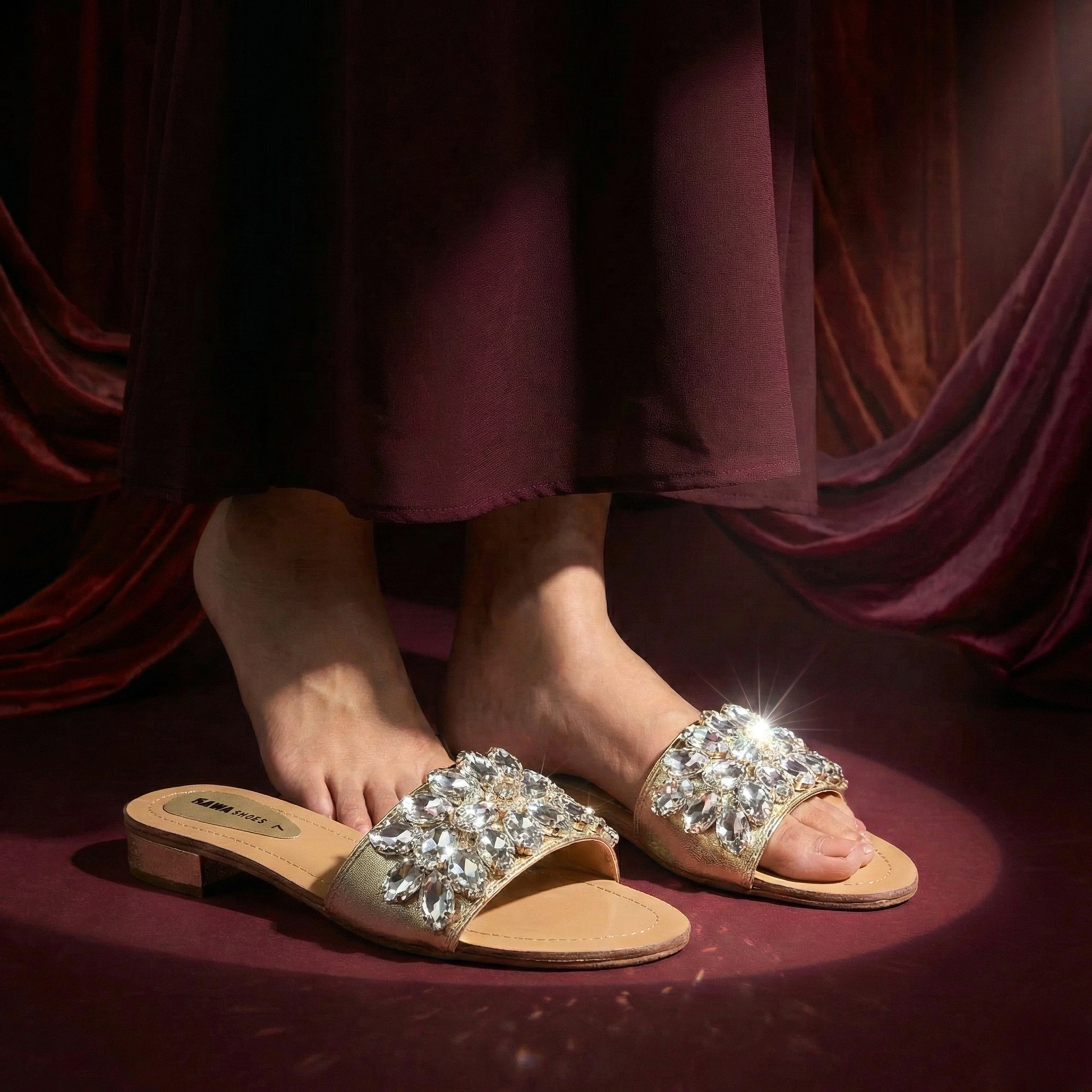 Gold sandals with rhinestone embellishments worn by a person sitting on a red fabric background.