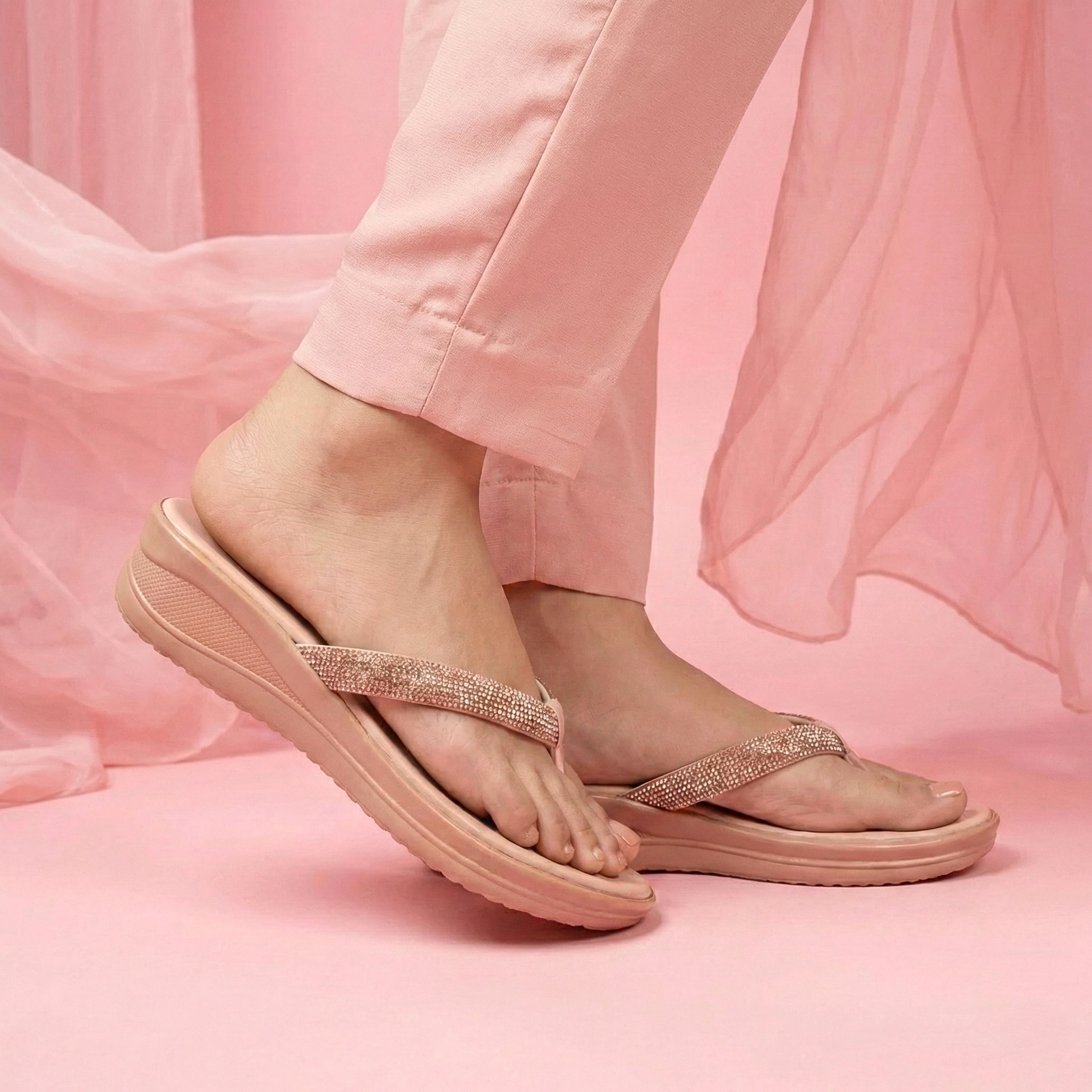 Beige sandals with glittery straps worn by a person on a pink background