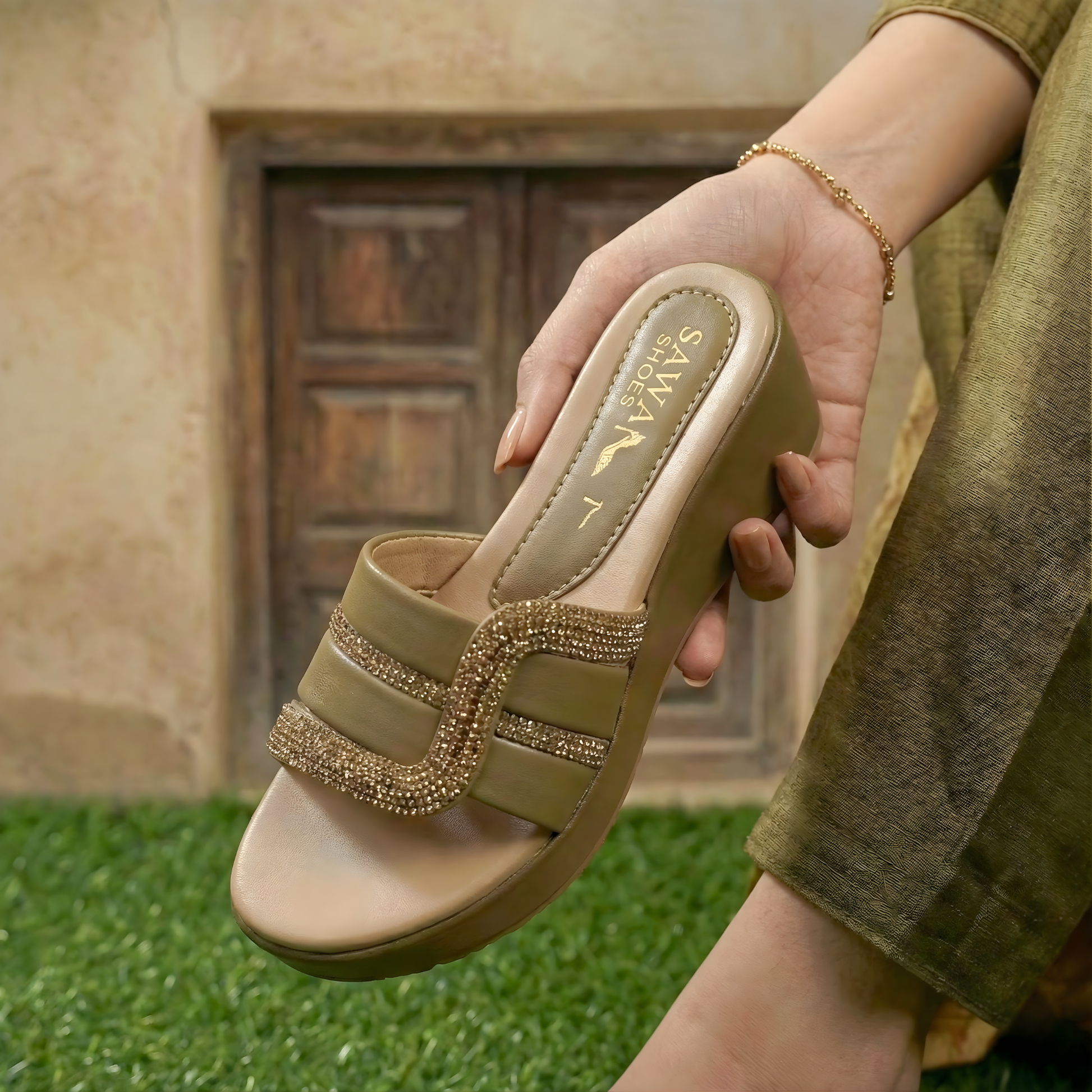 Beige sandal with embellishments held by a person on grass