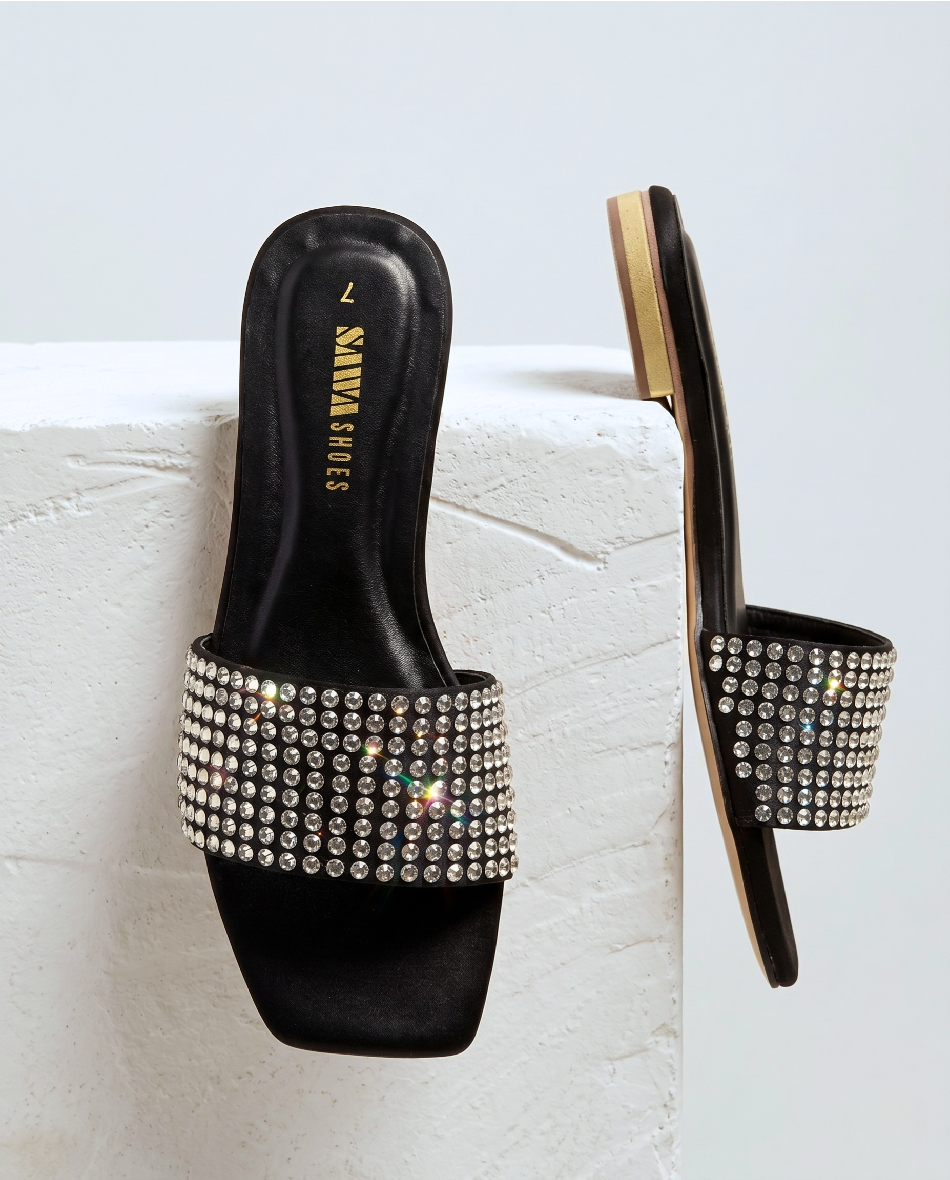 Black slide sandals with rhinestone embellishments on a light gray background