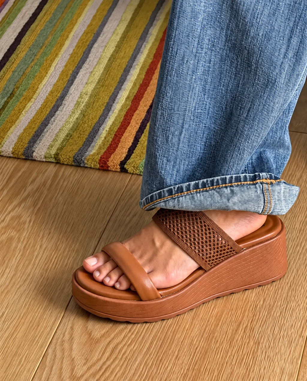 Tan wedge slides worn with jeans on a wooden floor