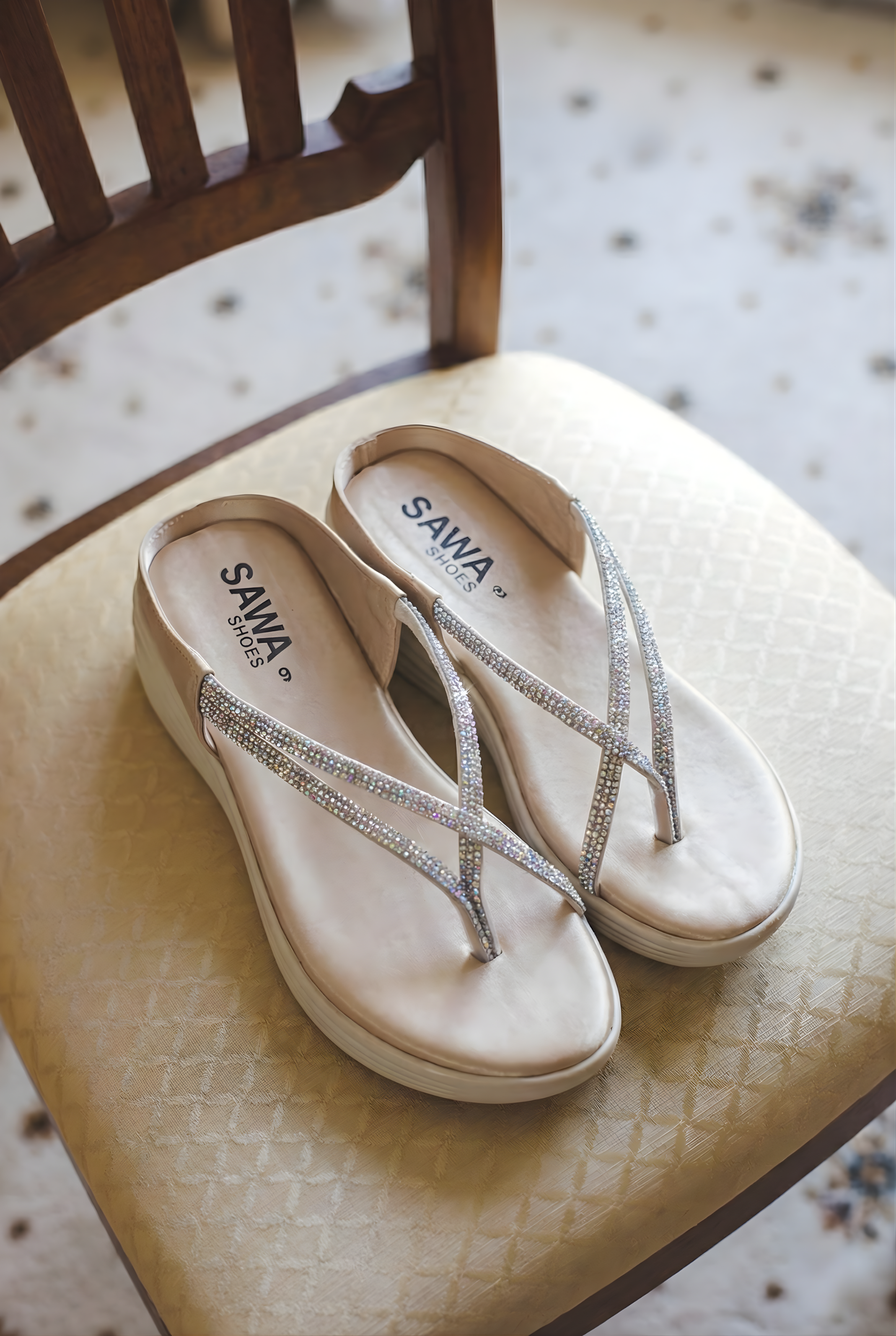Pair of SAWA Shoes cream platform thong sandals featuring silver crystal embellishments sitting on a beige chair