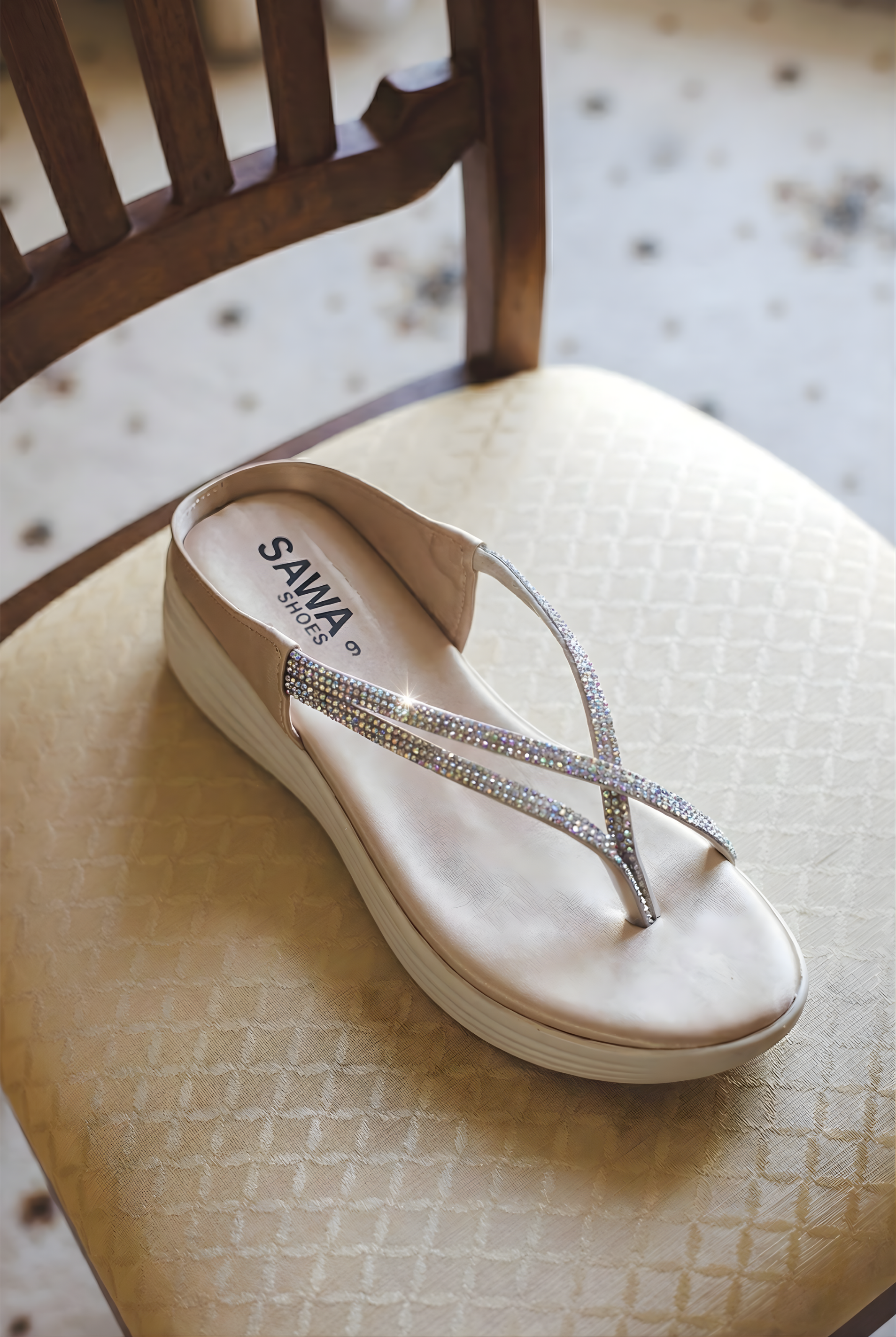 Pair of SAWA Shoes cream platform thong sandals featuring silver crystal embellishments sitting on a beige chair