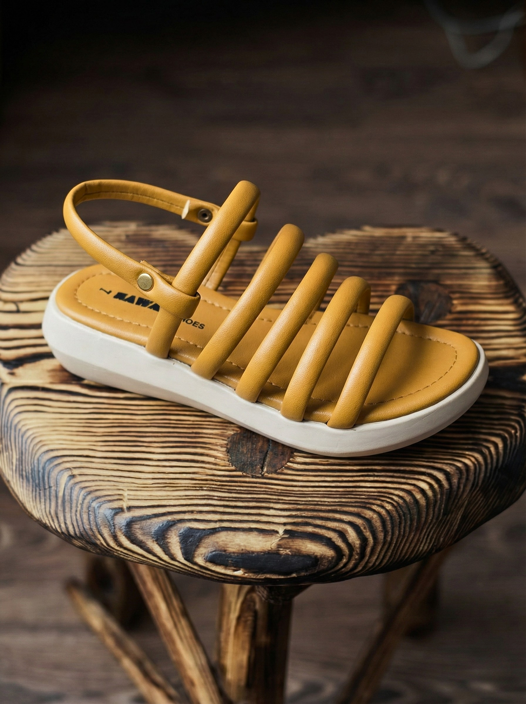 Woman wearing mustard yellow ochre sandals with puffy tubular straps and white flatform sole, sitting on a wooden stool. Stylish comfortable ladies footwear for summer in Pakistan
