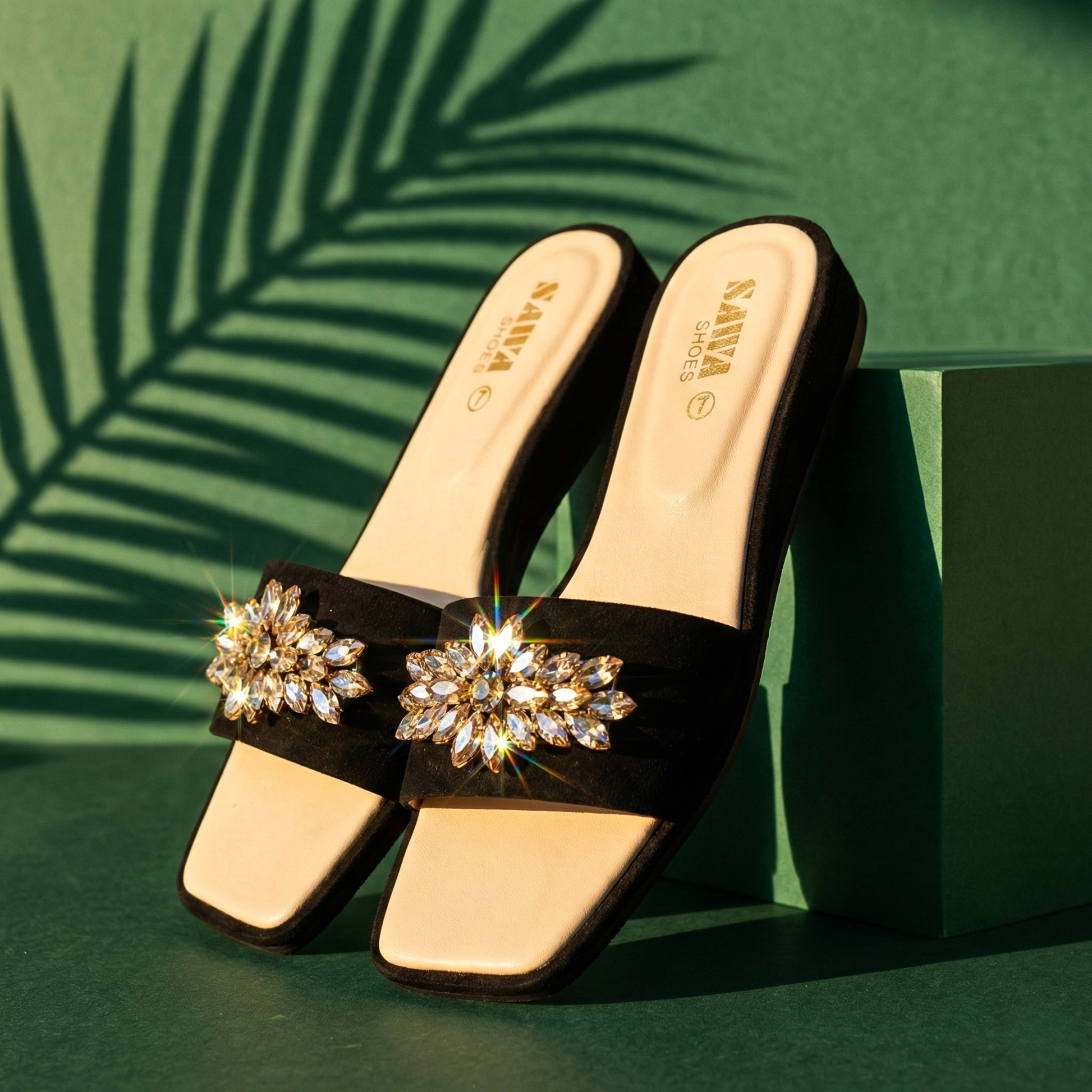 Close-up of black suede-strap sandals featuring a sparkling rhinestone brooch, beige cushioned insole, and modest wedge heel