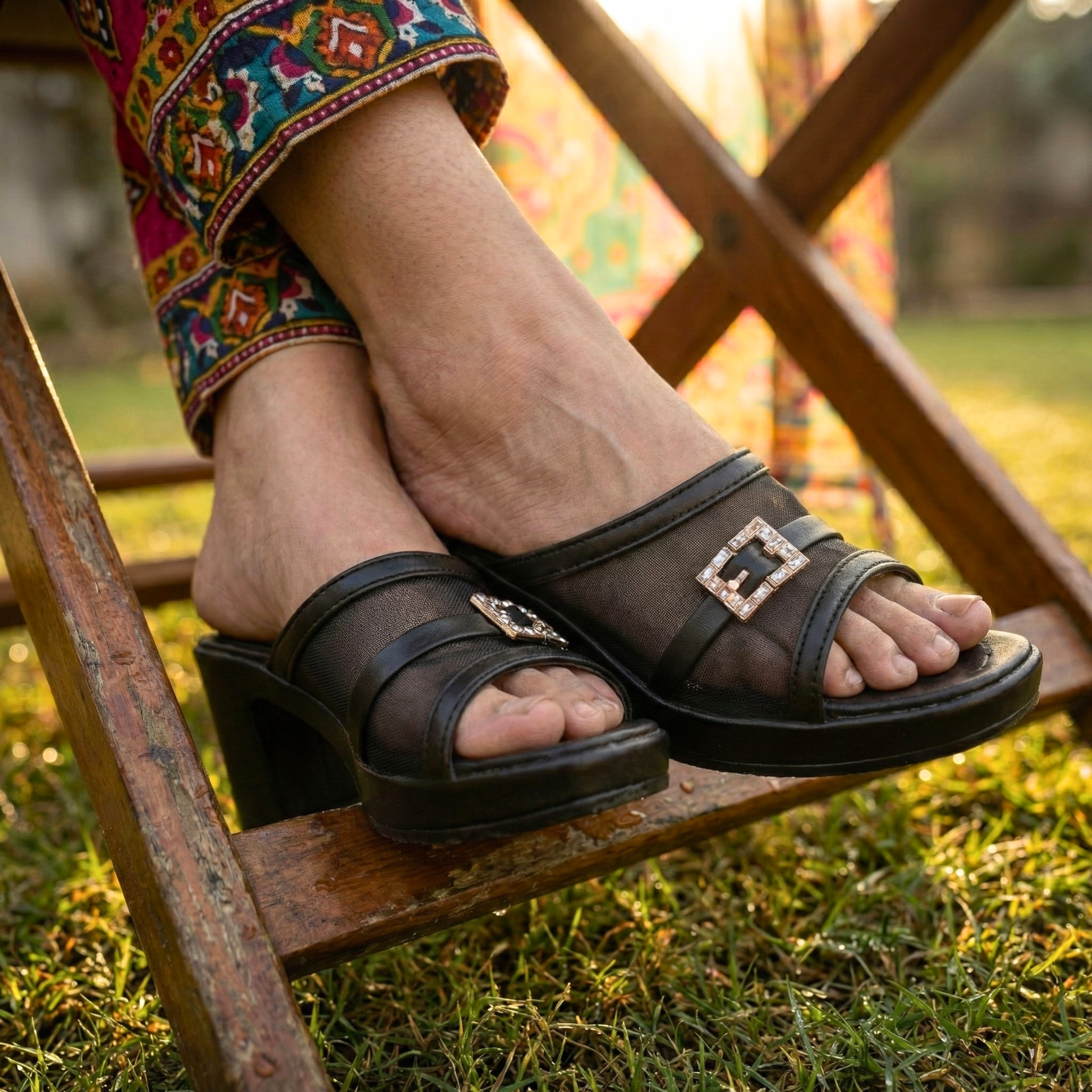 Pair of black sheer mesh block heels featuring a sparkling jewel buckle and comfortable platform sole, styled with patterned lawn trousers