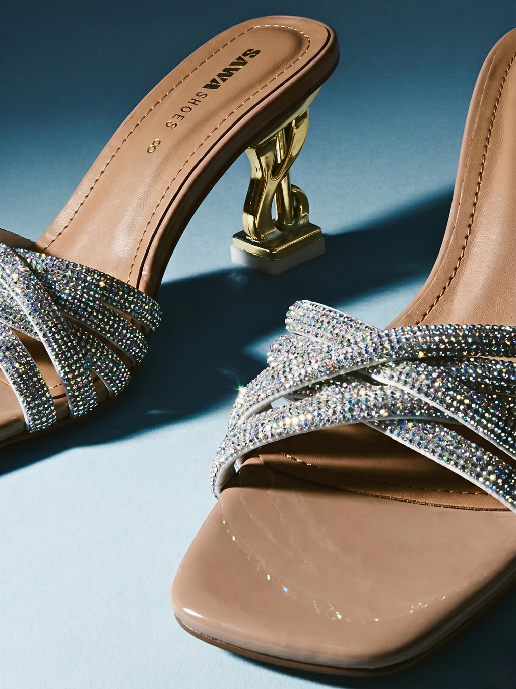 Beige high-heeled sandals with crystal embellishments on a blue background