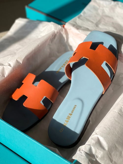 Burnt-orange cutout strap flat sandals with a sky-blue footbed inside a shoebox.