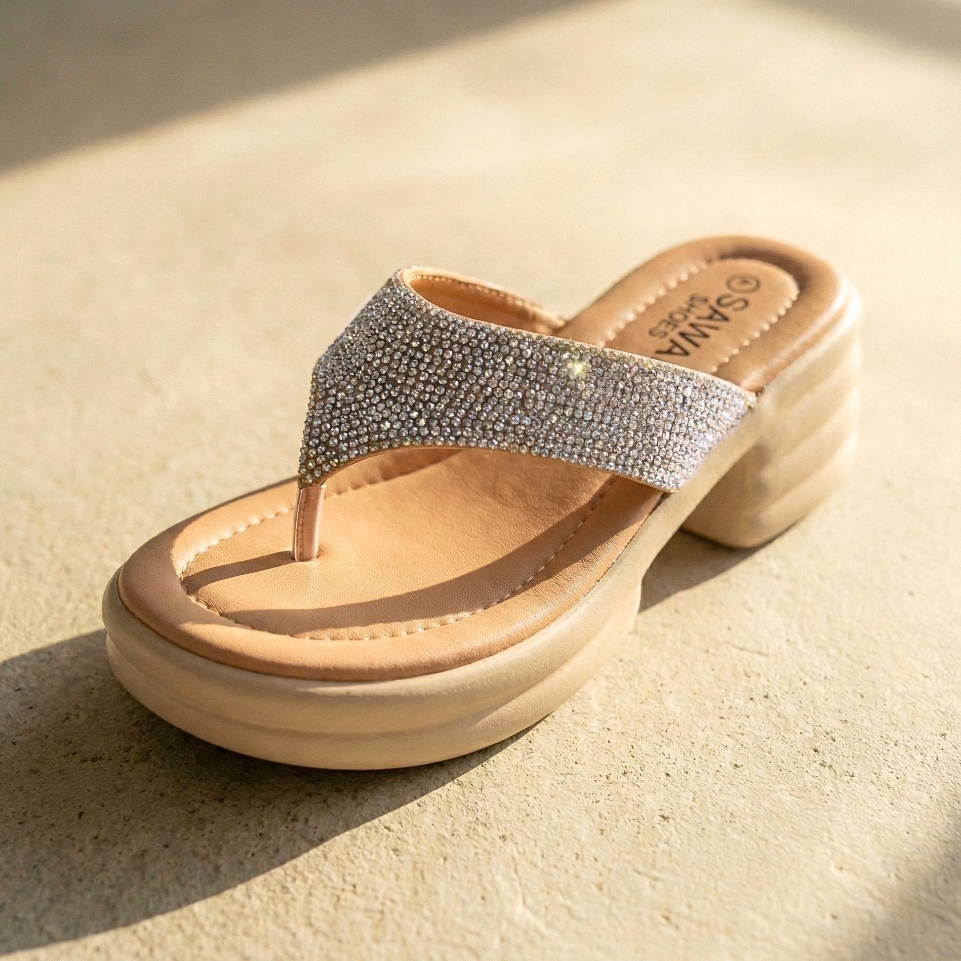 Beige sandal with rhinestone strap on a beige surface