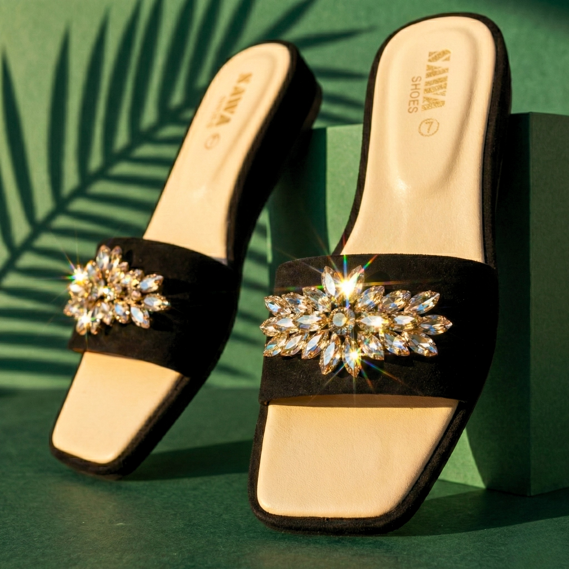 Black sandals with decorative rhinestone straps on a green background