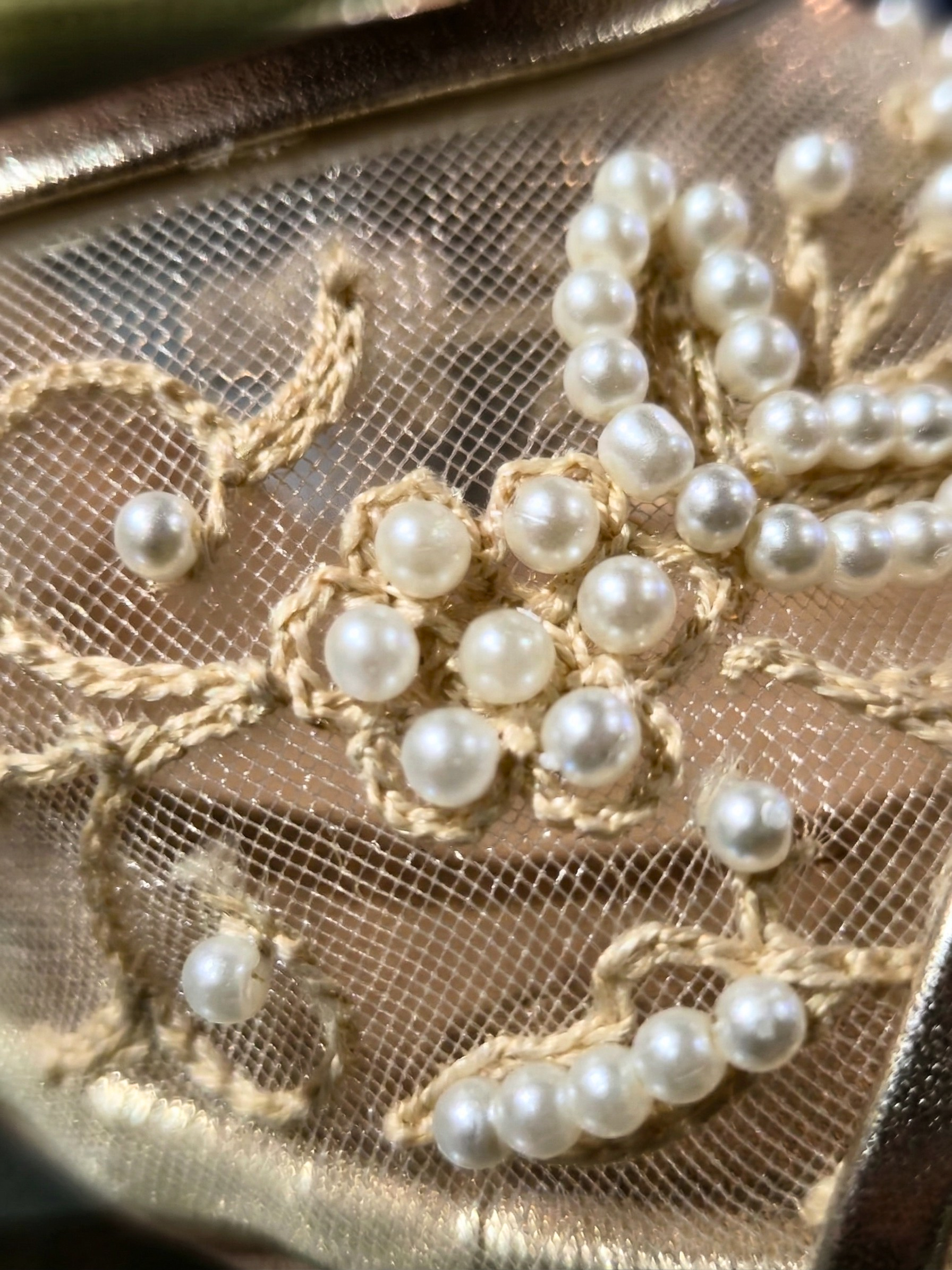 Macro close-up of intricate hand-stitched floral embroidery and pearls on mesh fabric