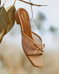 Top view of SAWA Shoes nude mesh bow mule featuring a square toe and gold logo on the footbed, laid on concrete