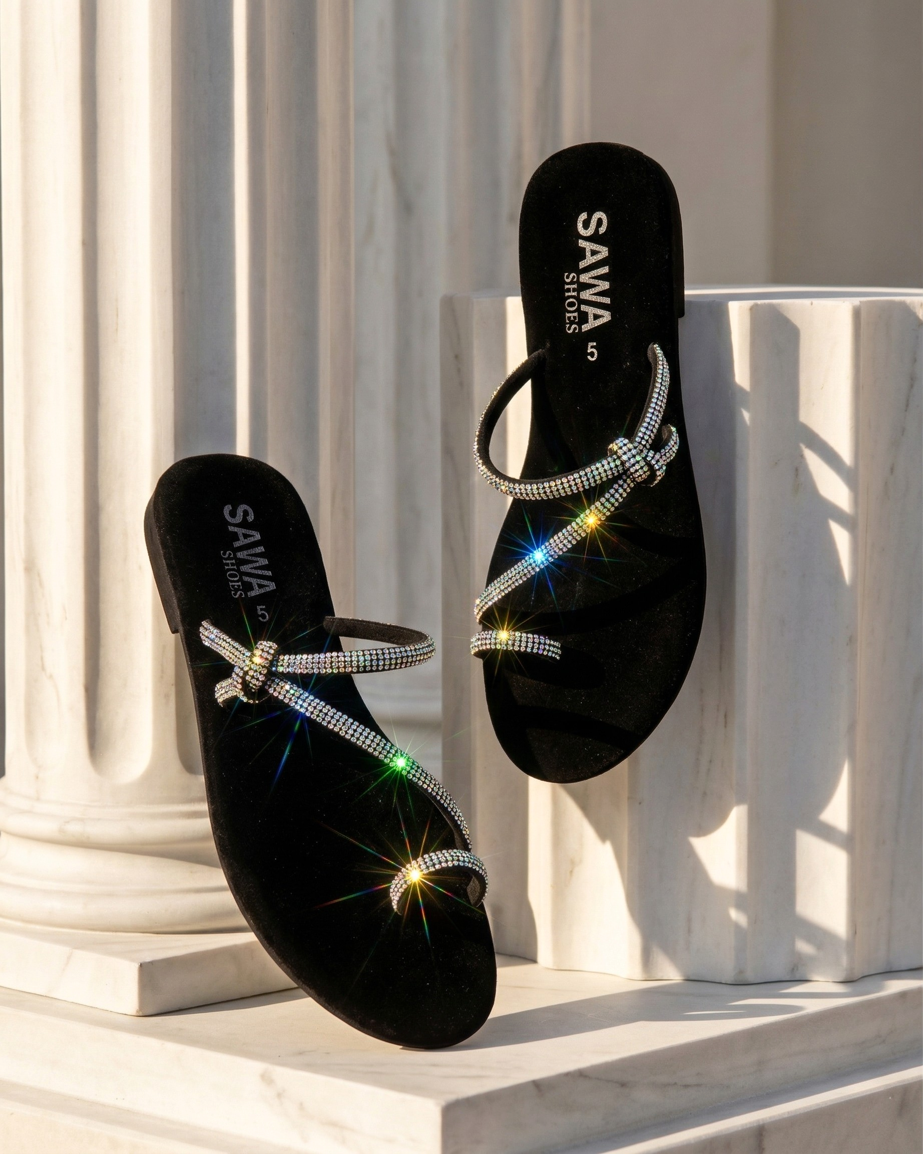 SAWA black velvet slides with sparkling rhinestone straps and a decorative knot detail, displayed against white marble columns
