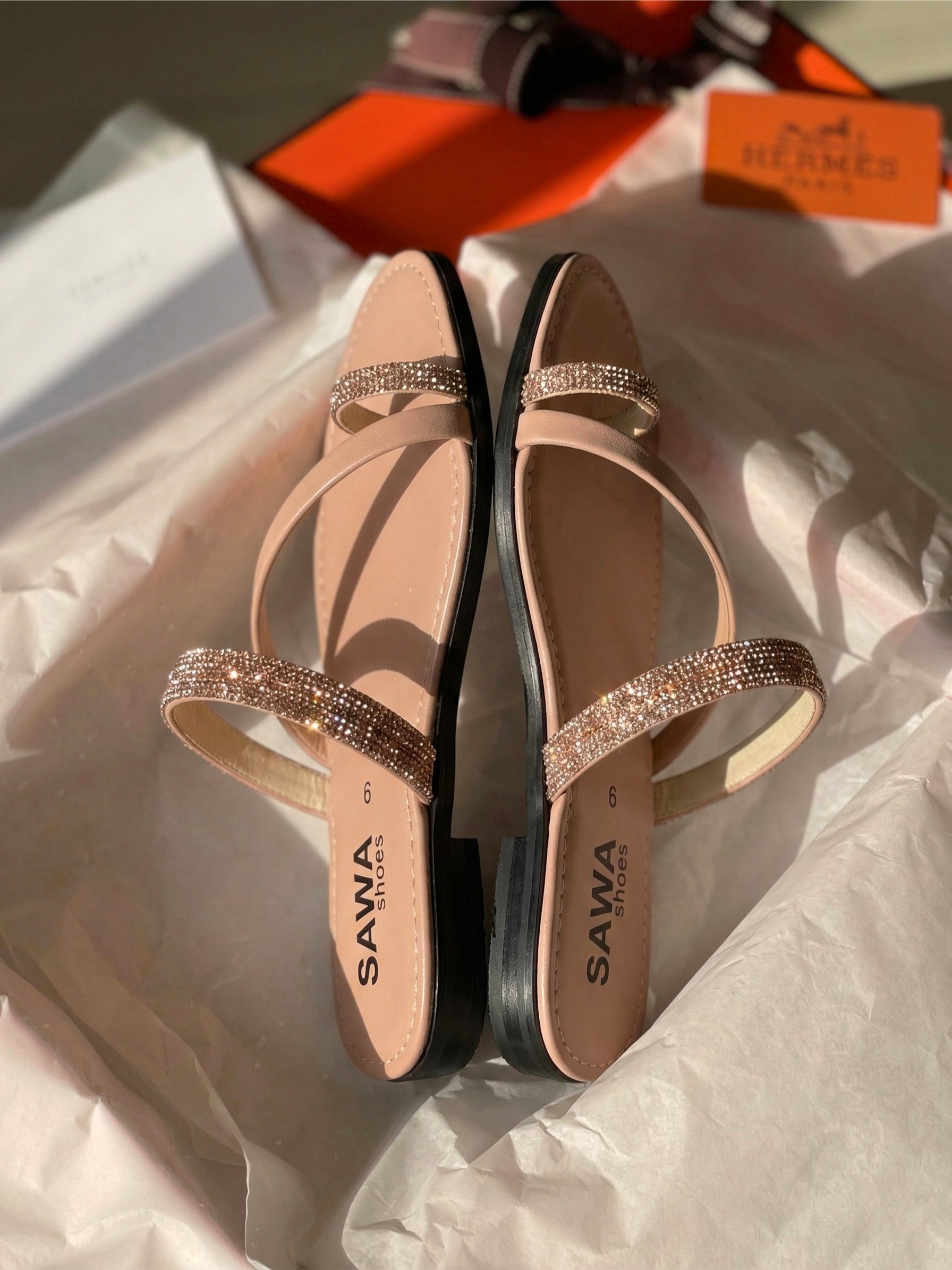 Nude flat sandals with rhinestone embellished straps and toe-ring design on white tissue paper background.