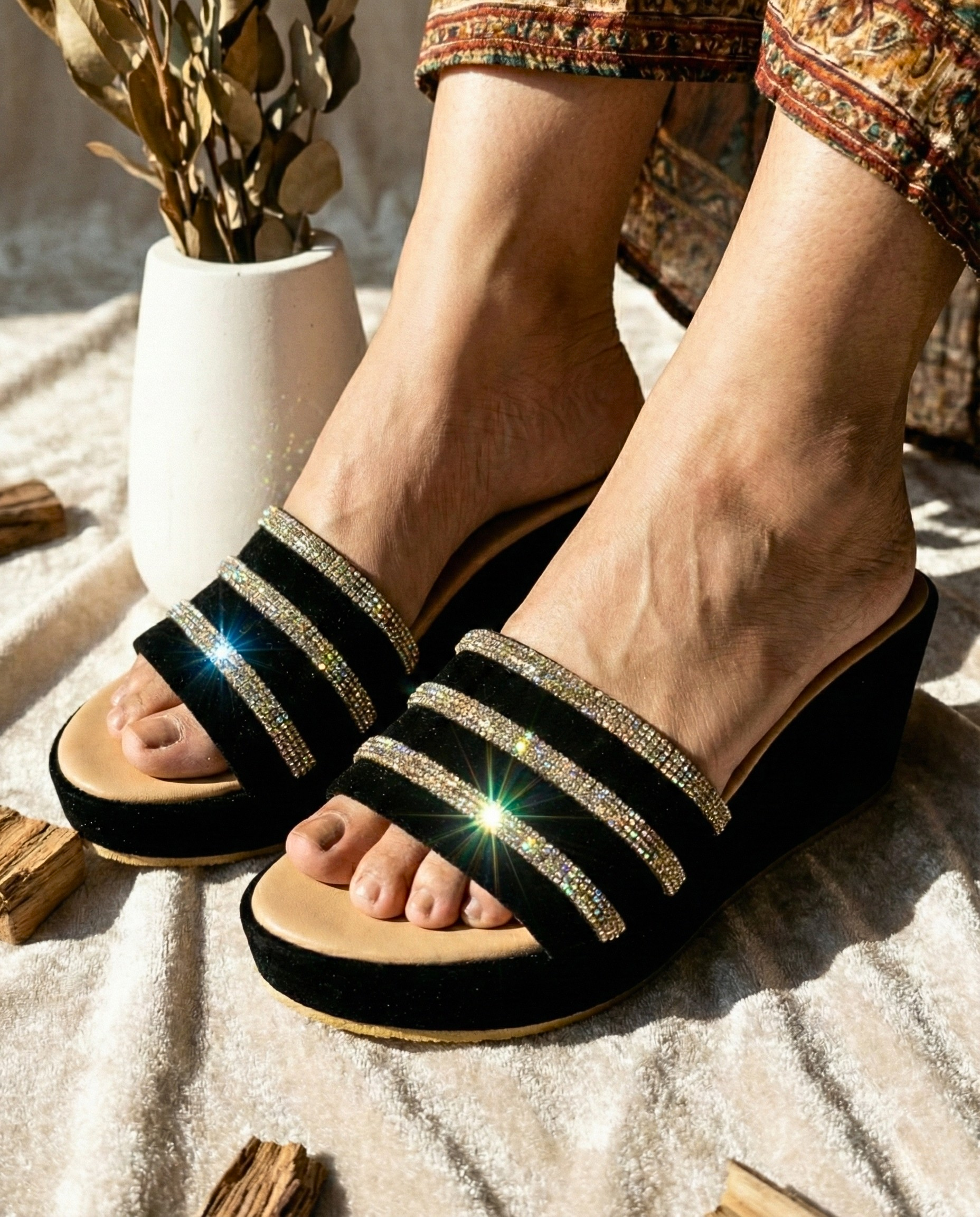 Detailed close-up of gold and silver rhinestone embellishments on black velvet straps of a formal wedge sandal