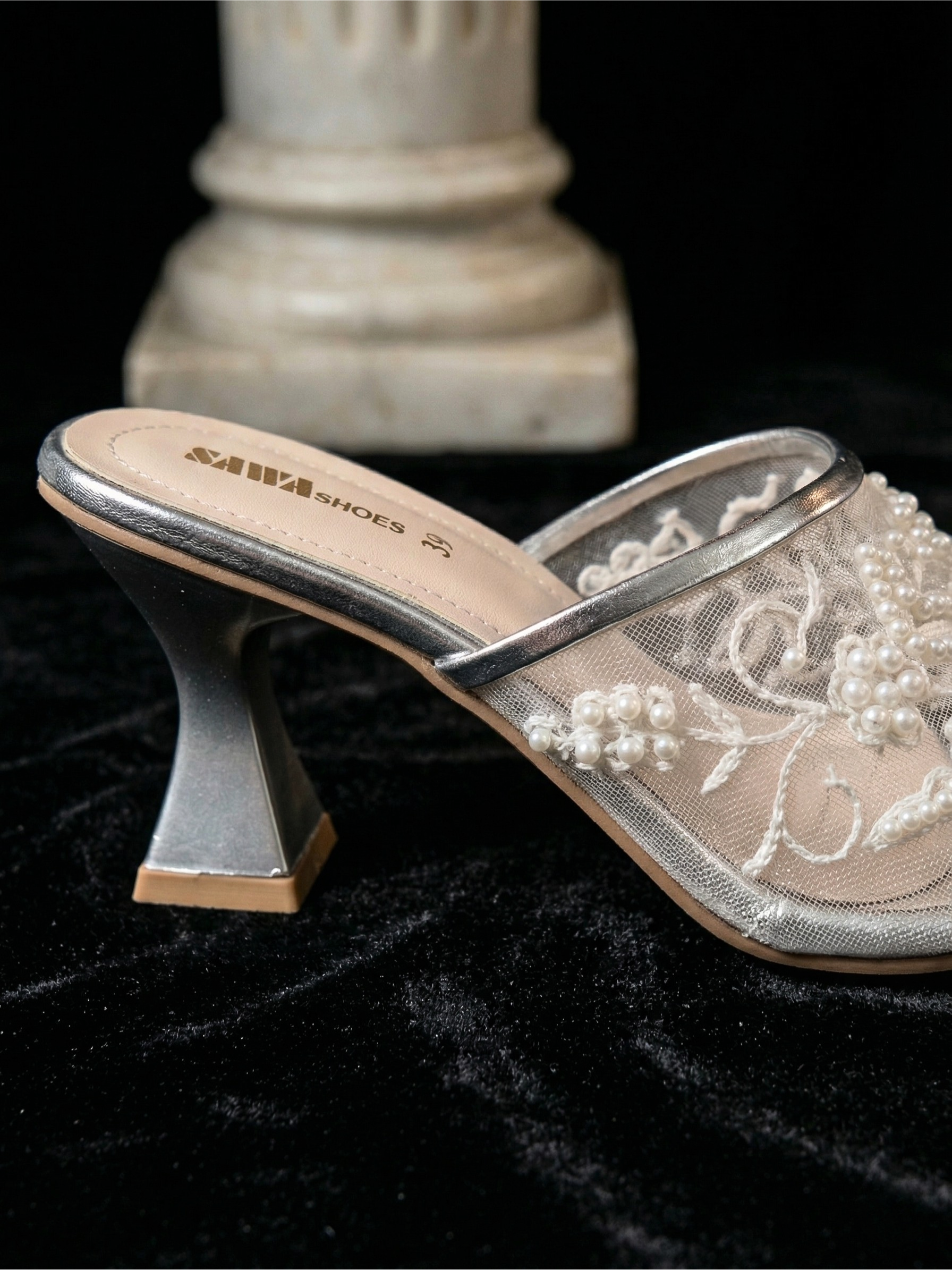 Side view of metallic silver mesh mules showing the architectural flared block heel and pearl embellishments.