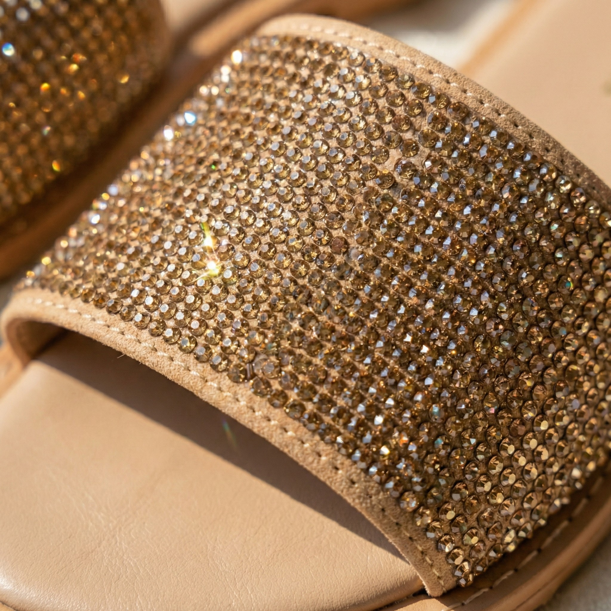 Macro shot of densely packed champagne-gold rhinestones on a sandal strap showing high-brilliance shimmer