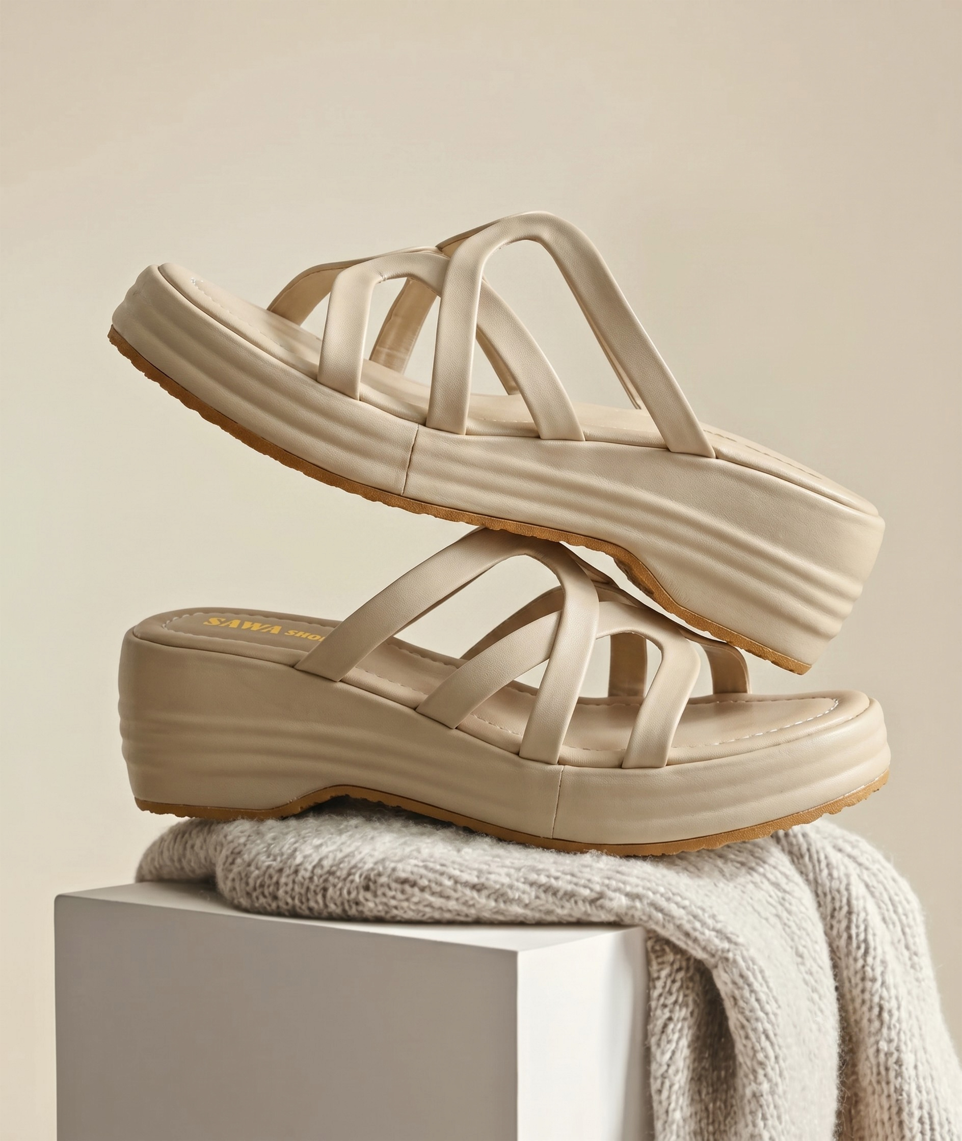 Two cream-colored women's wedge slides stacked creatively on top of each other over a grey knit blanket.