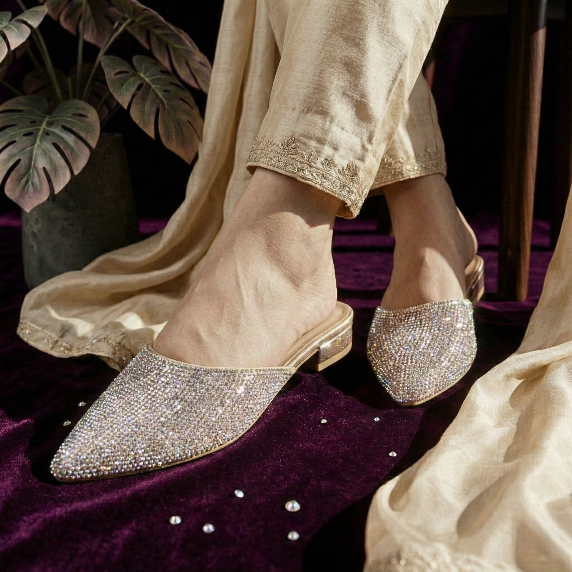 Close-up of a person wearing gold-toned Starry Night crystal mules with an embroidered Pakistani silk suit on a purple velvet background