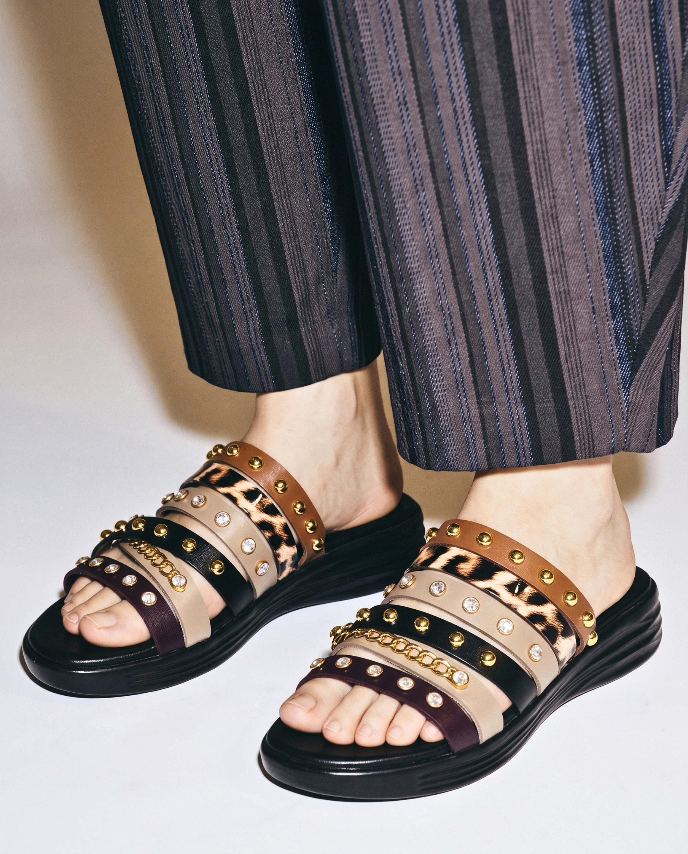 Multi-strap women's slide sandals featuring a leopard print band, studded leather-look straps, crystal accents, and a contoured black footbed